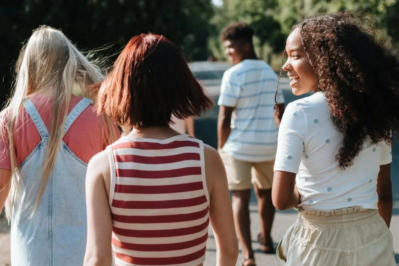 Group of young people casually socializing outdoors, with three women in the foreground and two men in the background.