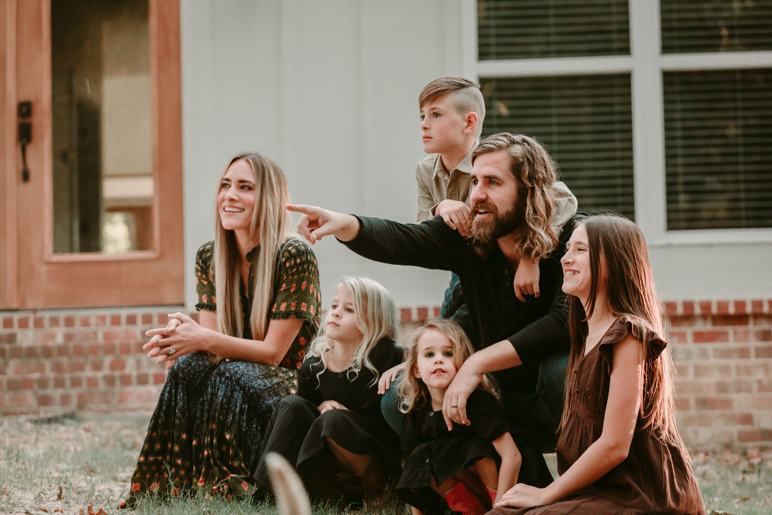 A family sitting outdoors, with two adults and four children, smiling and looking in the same direction.
