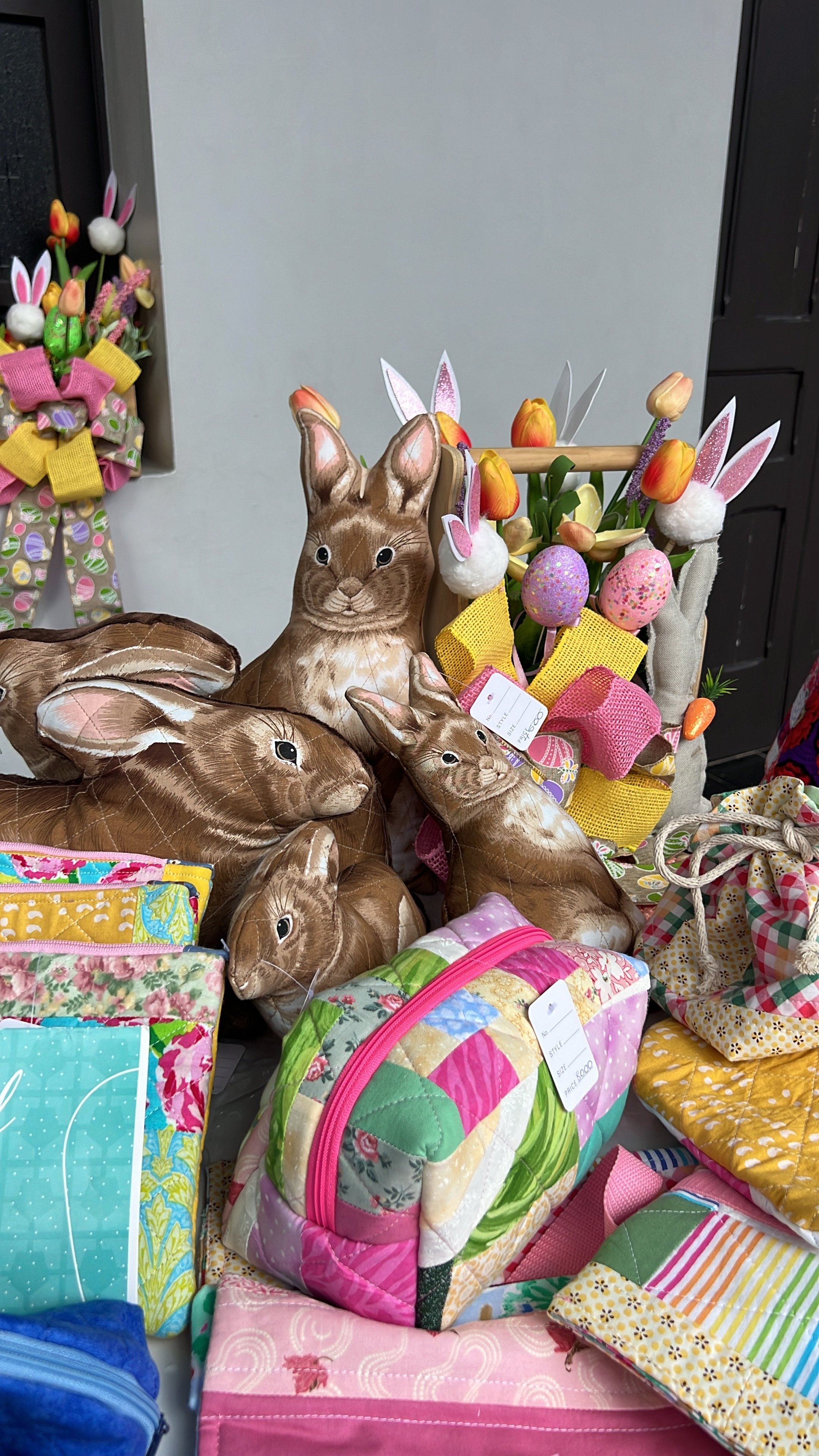 Mesa decorativa con conejos de peluche, flores de tulipán y huevos de Pascua. También hay bolsas de tela coloridas y cojines con estampados variados.