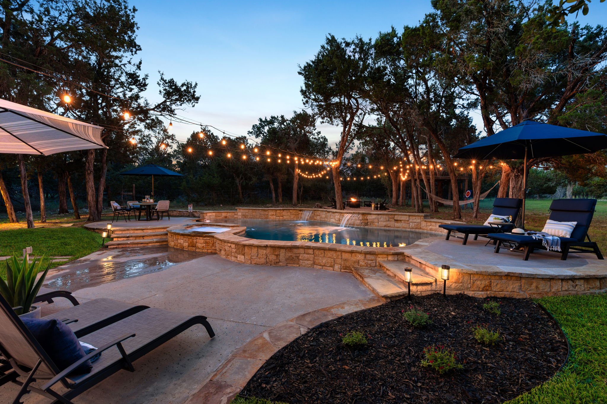 Evening bliss with Waterfall pool & heated spa with lounge chairs and an abundance of ambient lighting.