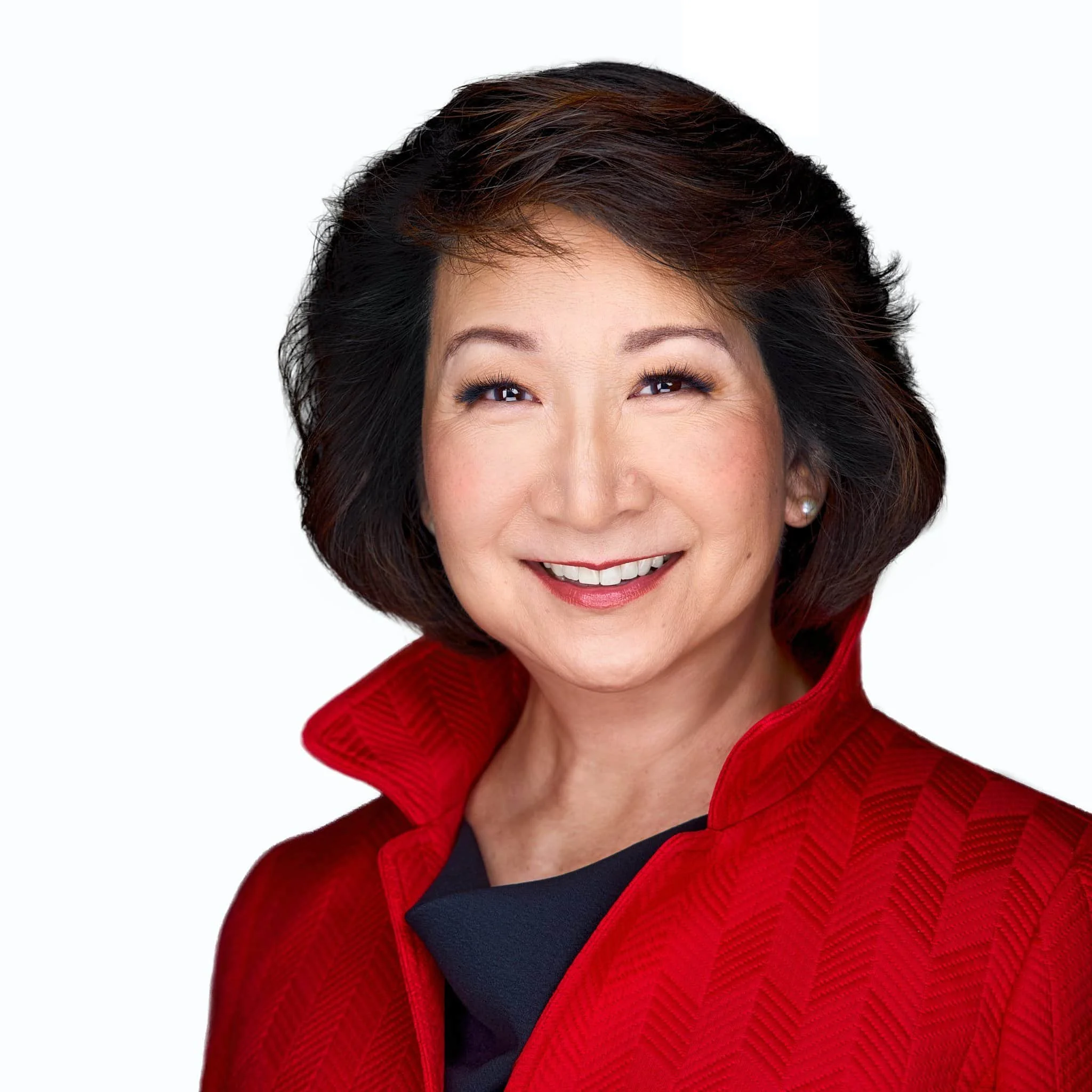 Professional headshot of a woman wearing a bold red blazer over a black top, smiling confidently against a clean white background. Her dark hair is styled neatly, and she faces the camera with a warm, approachable expression.