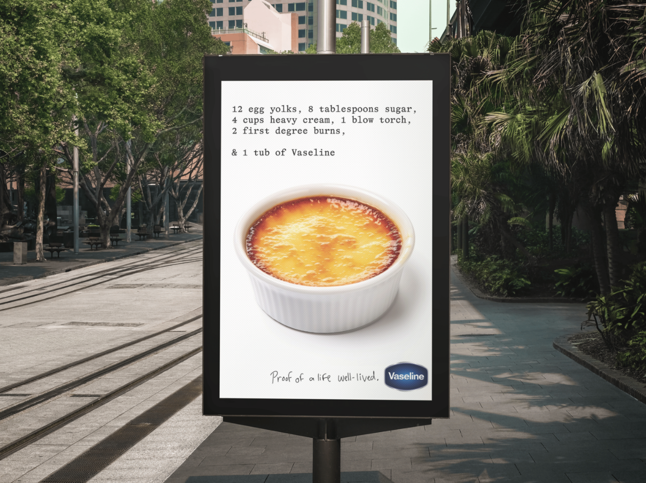 Billboard displaying a crème brûlée dessert with recipe ingredients and the Vaseline logo. The background includes trees, high-rise buildings, and a sidewalk.