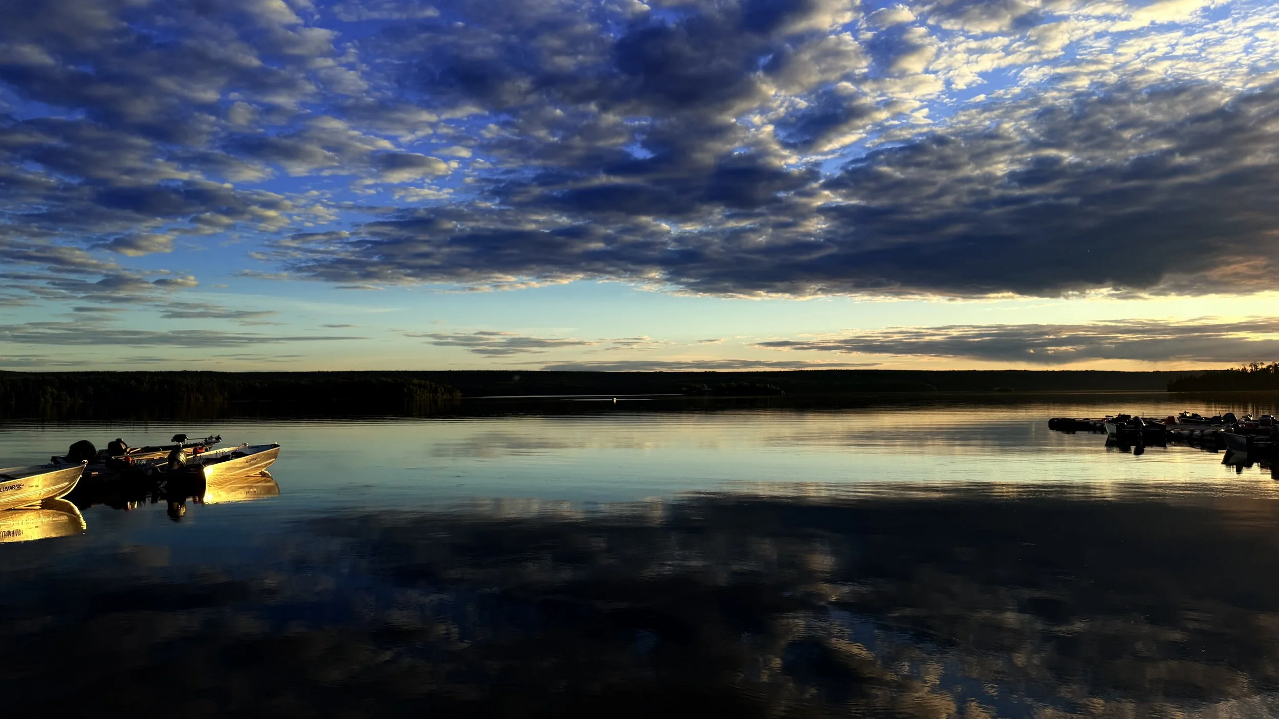 Boats docked on a calm lake during sunset with a cloudy sky overhead.