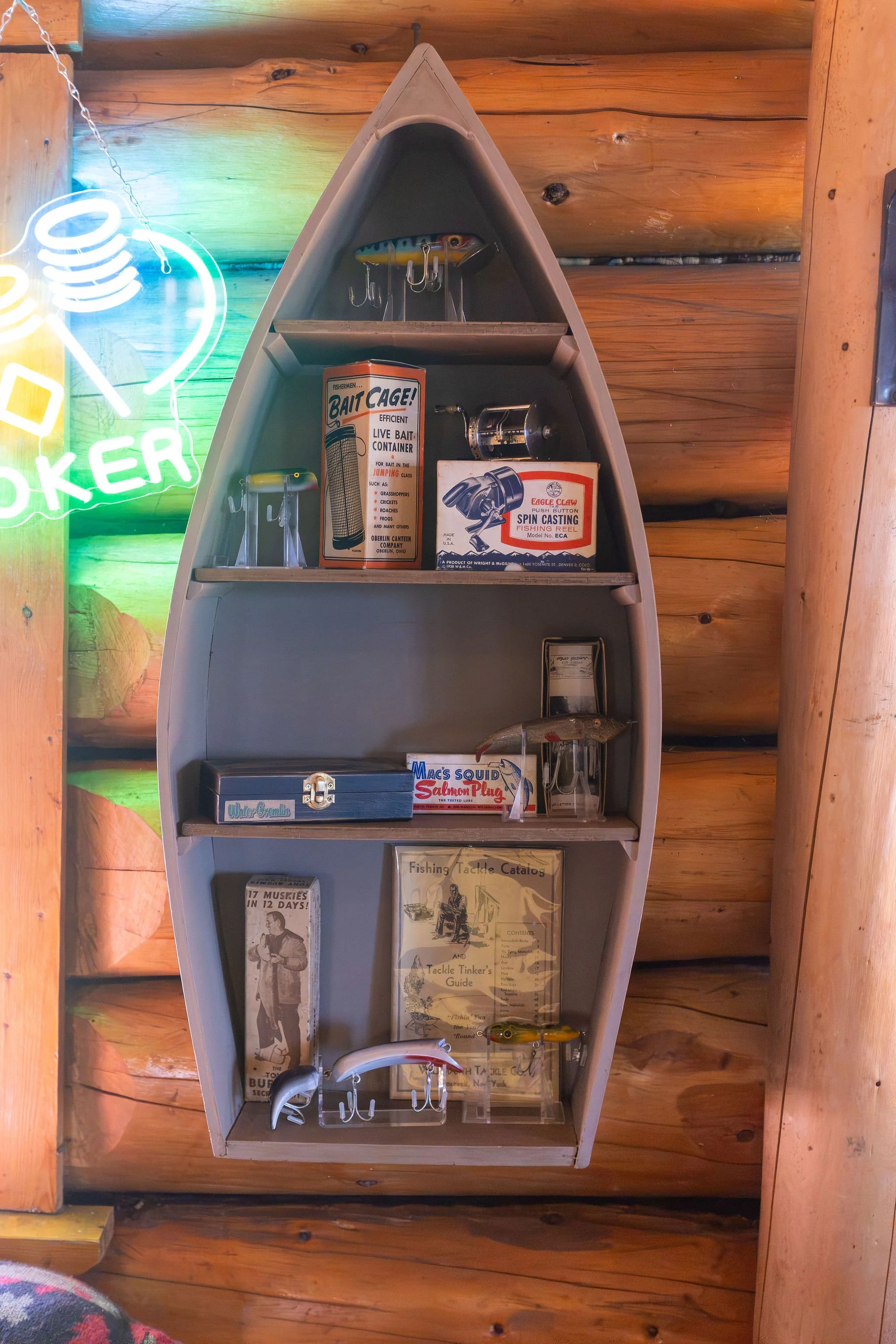 Inside a wooden boat-shaped display shelf containing various fishing-related items such as fishing lures, catalogs, and fishing tackle guides. The background is wood paneling and there is a partial neon sign visible on the left side.