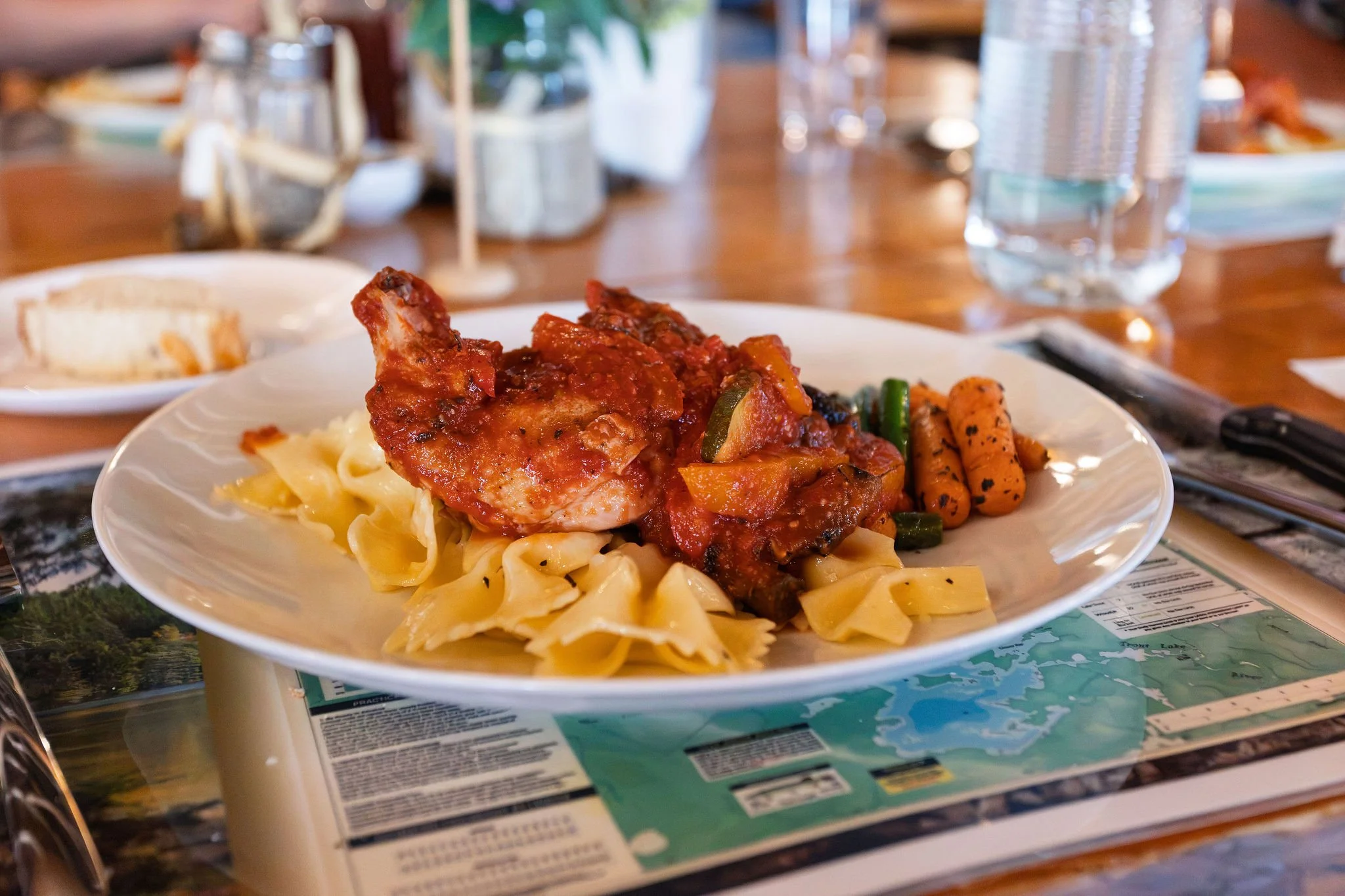 A plate of pasta with chicken and tomato sauce, garnished with vegetables, resting on a table at a restaurant or cafe.