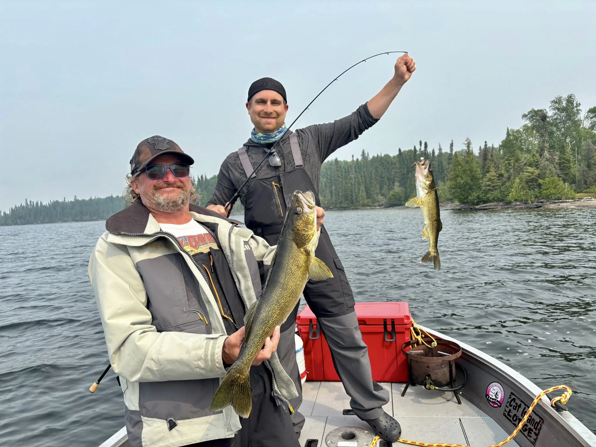 People gathering on a dock in trout lake with boats and a seaplane on a calm lake, surrounded by forested hills.