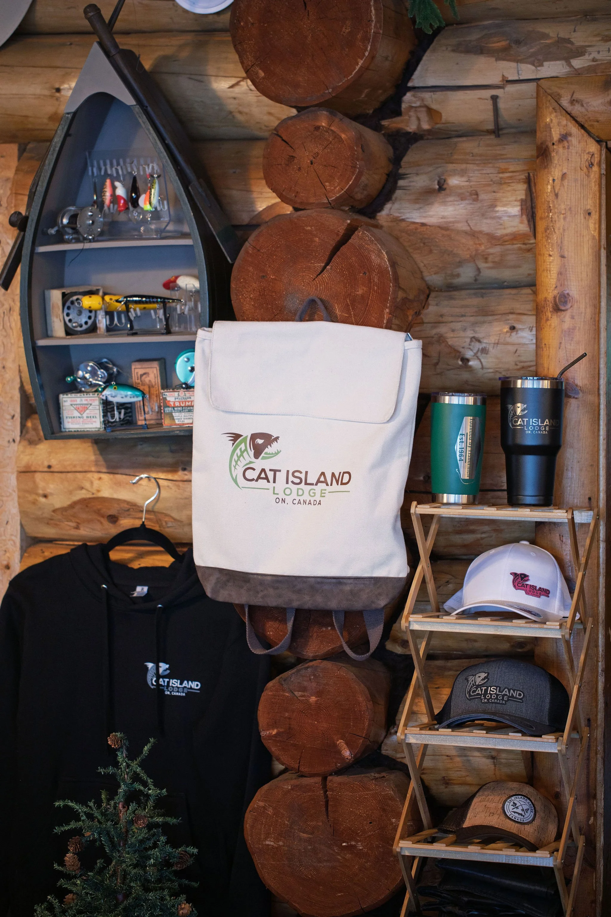 Display of fishing lures, hats, drinkware, and clothing with Cat Island Lodge branding on a wooden wall shelf in a rustic setting.