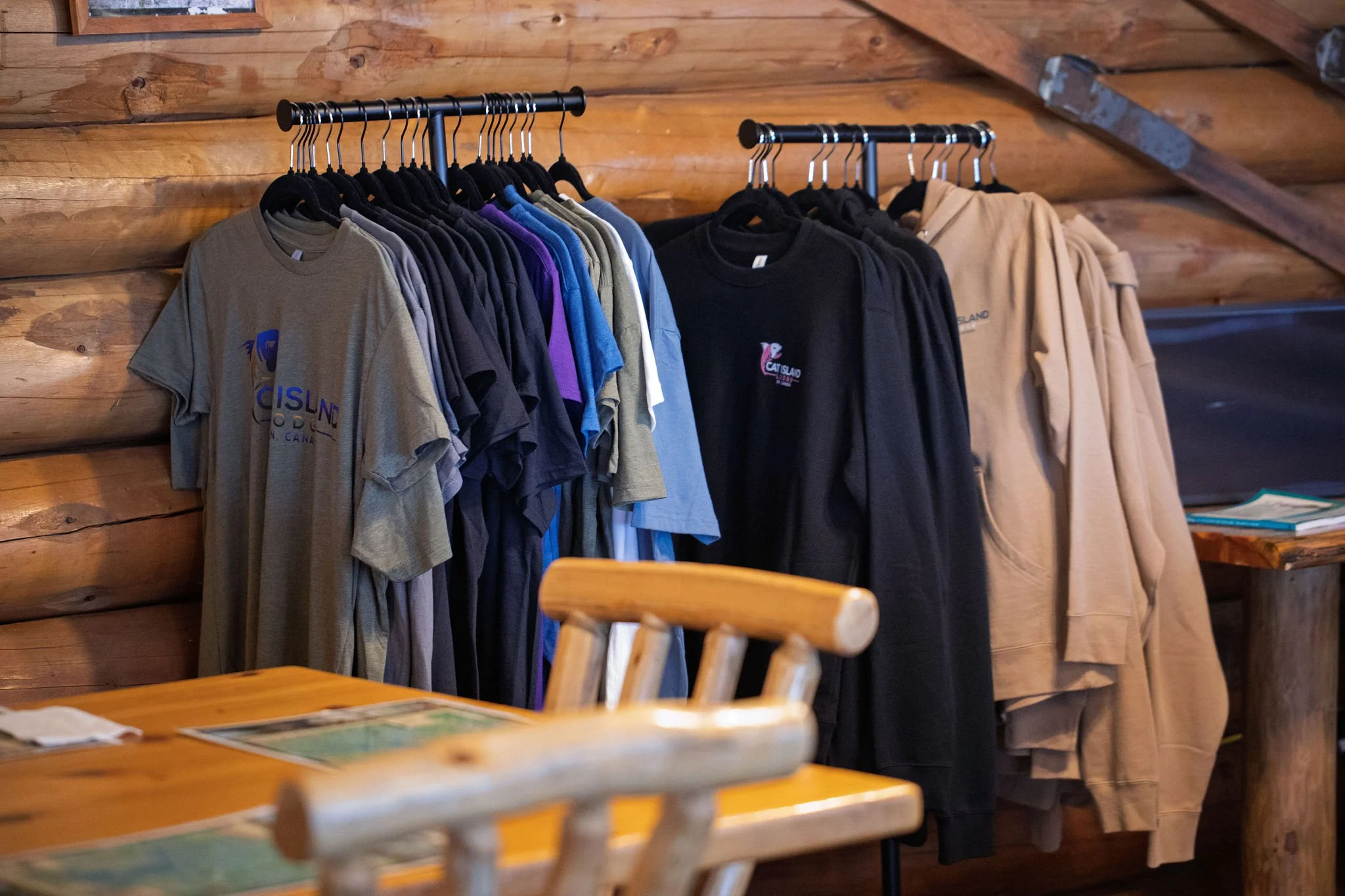 Clothing rack with various t-shirts in different colors hanging against a wooden wall in a rustic setting.
