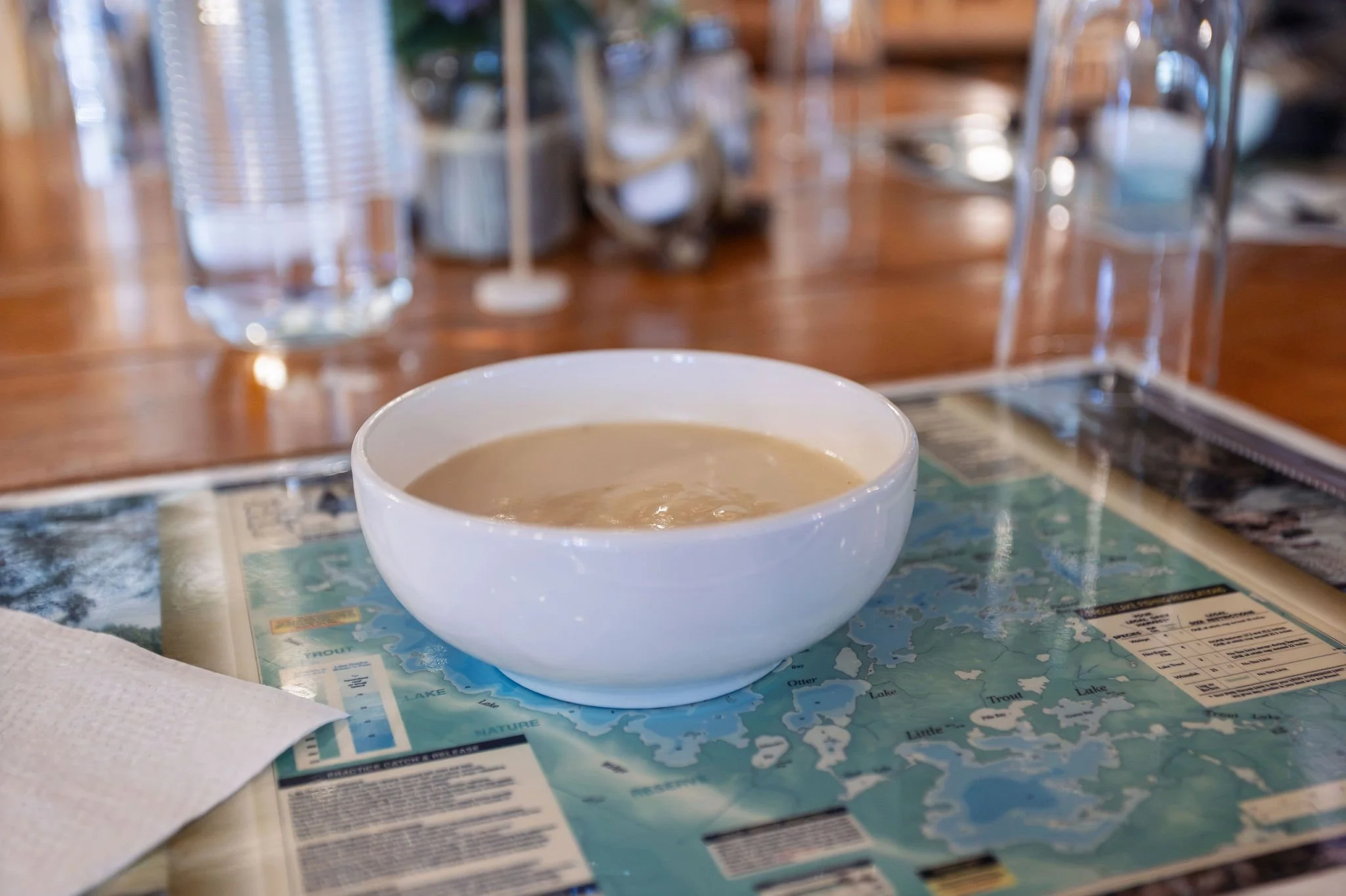 White cup of coffee on a printed map table at a restaurant with water glasses and condiment bottles in the background.