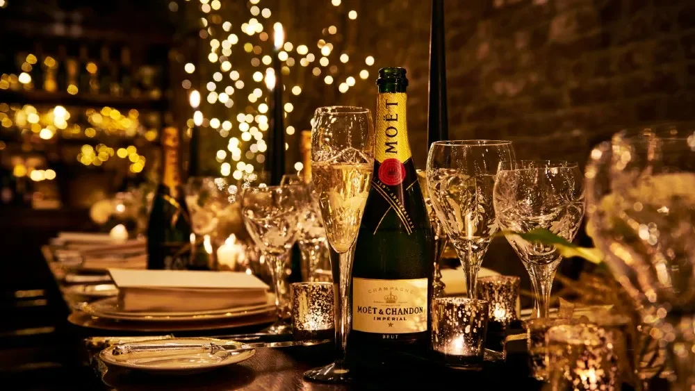 A table set for celebration with a bottle of Moët & Chandon champagne, glasses filled with bubbly, and decorative lighting creating a festive atmosphere.