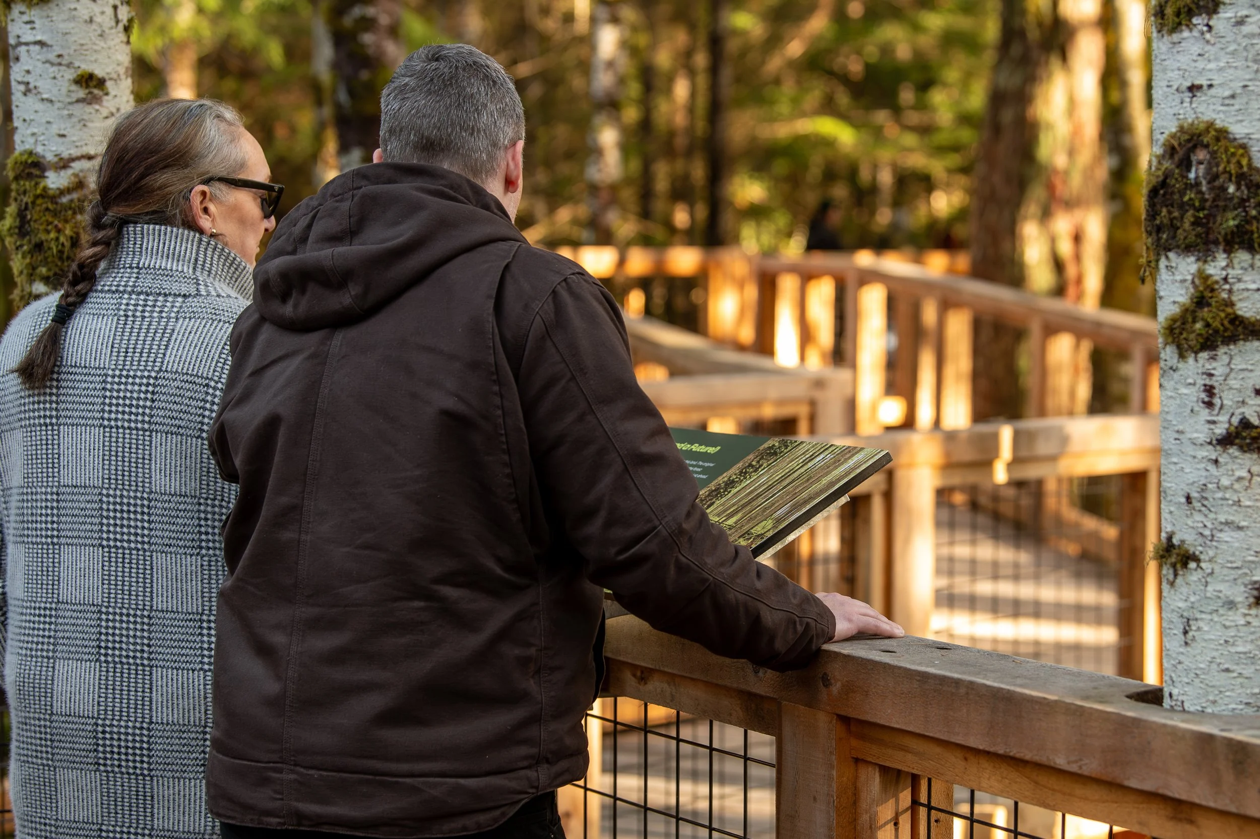 Male and female adults standing on the Squamish Canyon boardwalk reading a sign.
