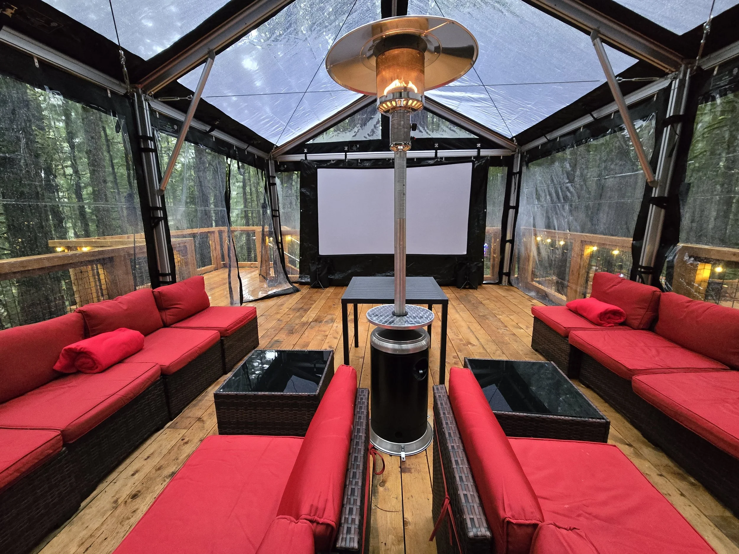 Outdoor cinema set inside a clear tent with a heater, surrounded by forest in Squamish Canyon.