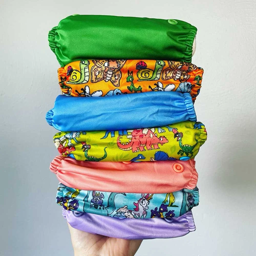 Stack of colorful cloth diapers with various patterns, including animals and cartoon designs, held in a hand.