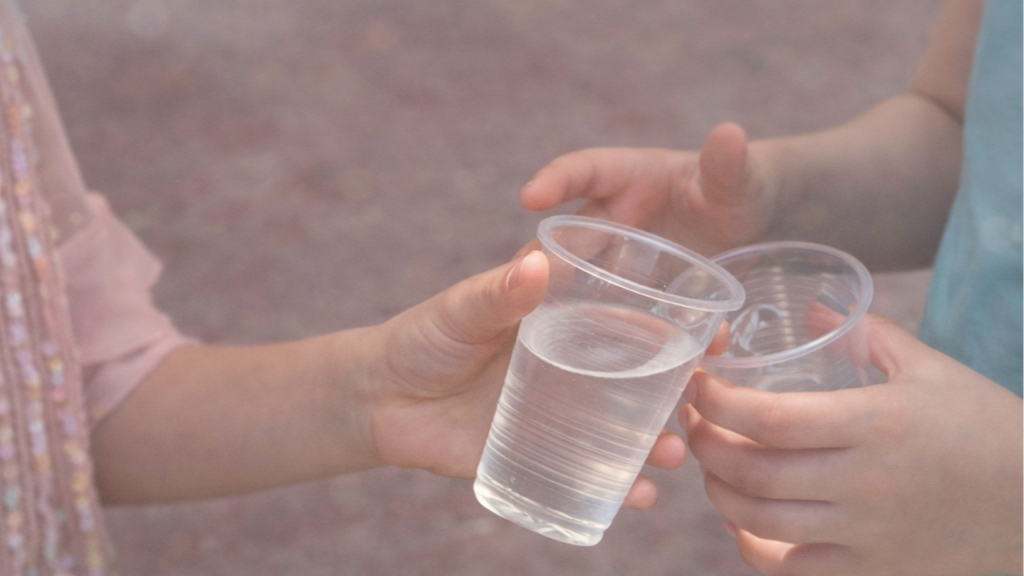 Children exchanging clear plastic cups filled with water outdoors.