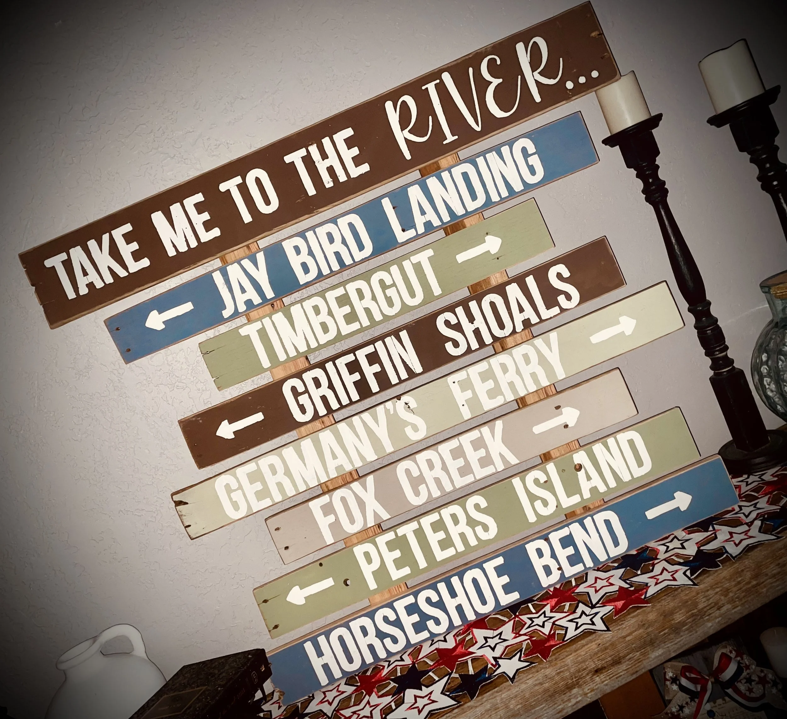 A multi-colored wooden signpost with directions and destinations for various locations, including Jay Bird Landing, Timbergutch, Griffin Shoals, Germania's Ferry, Fox Creek, Peters Island, Horseshore Bend, and a note to take me to the river.