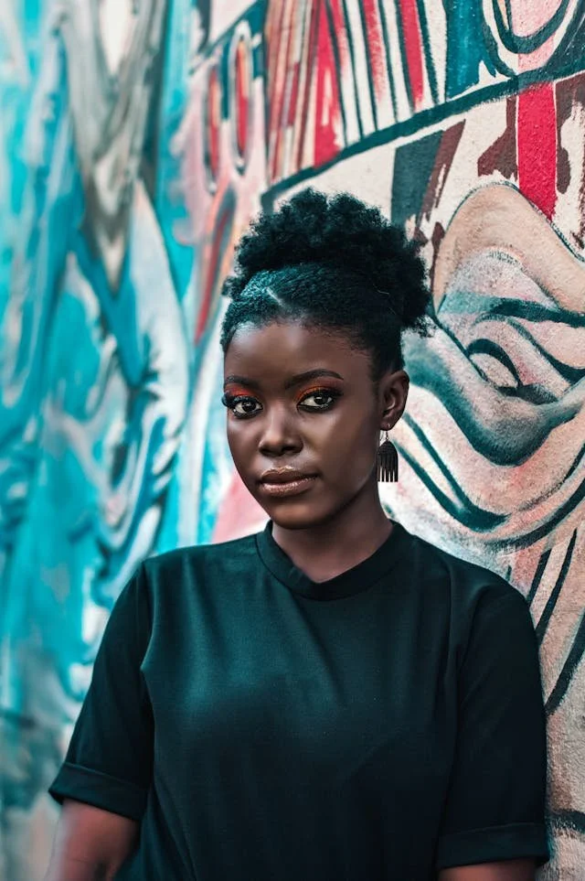 Young Black woman with natural curly hair and earrings standing against a colorful graffiti wall. Blueprint Studio Web Design Black owned