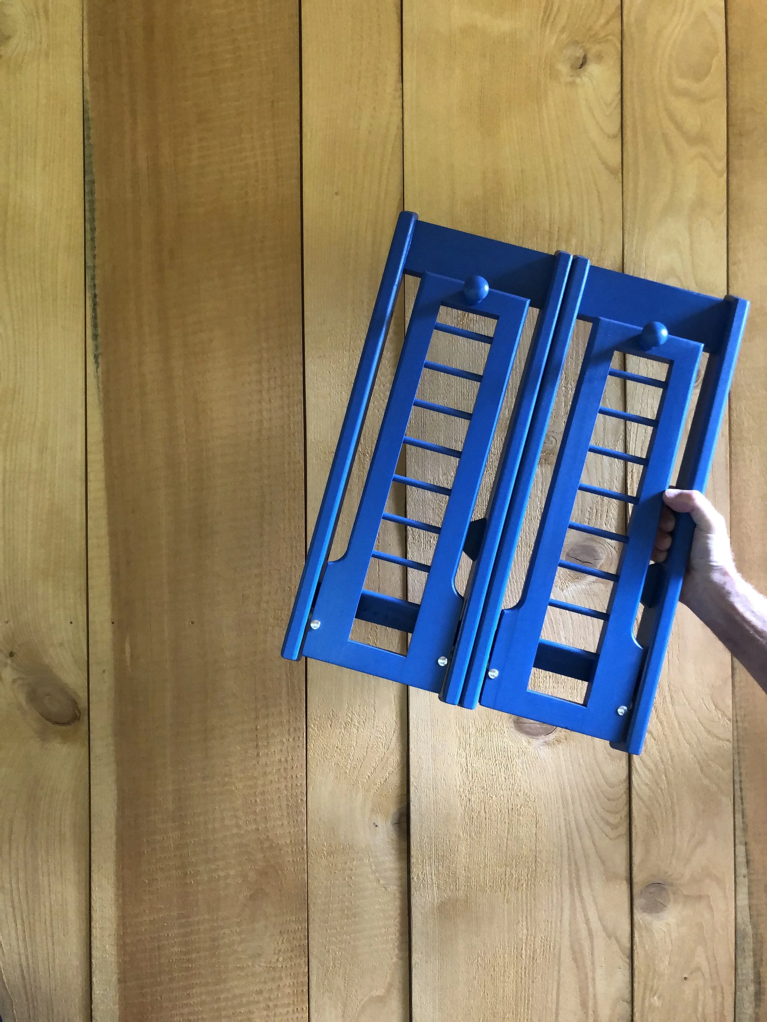 A person holding a blue folding chair against a wooden wall.