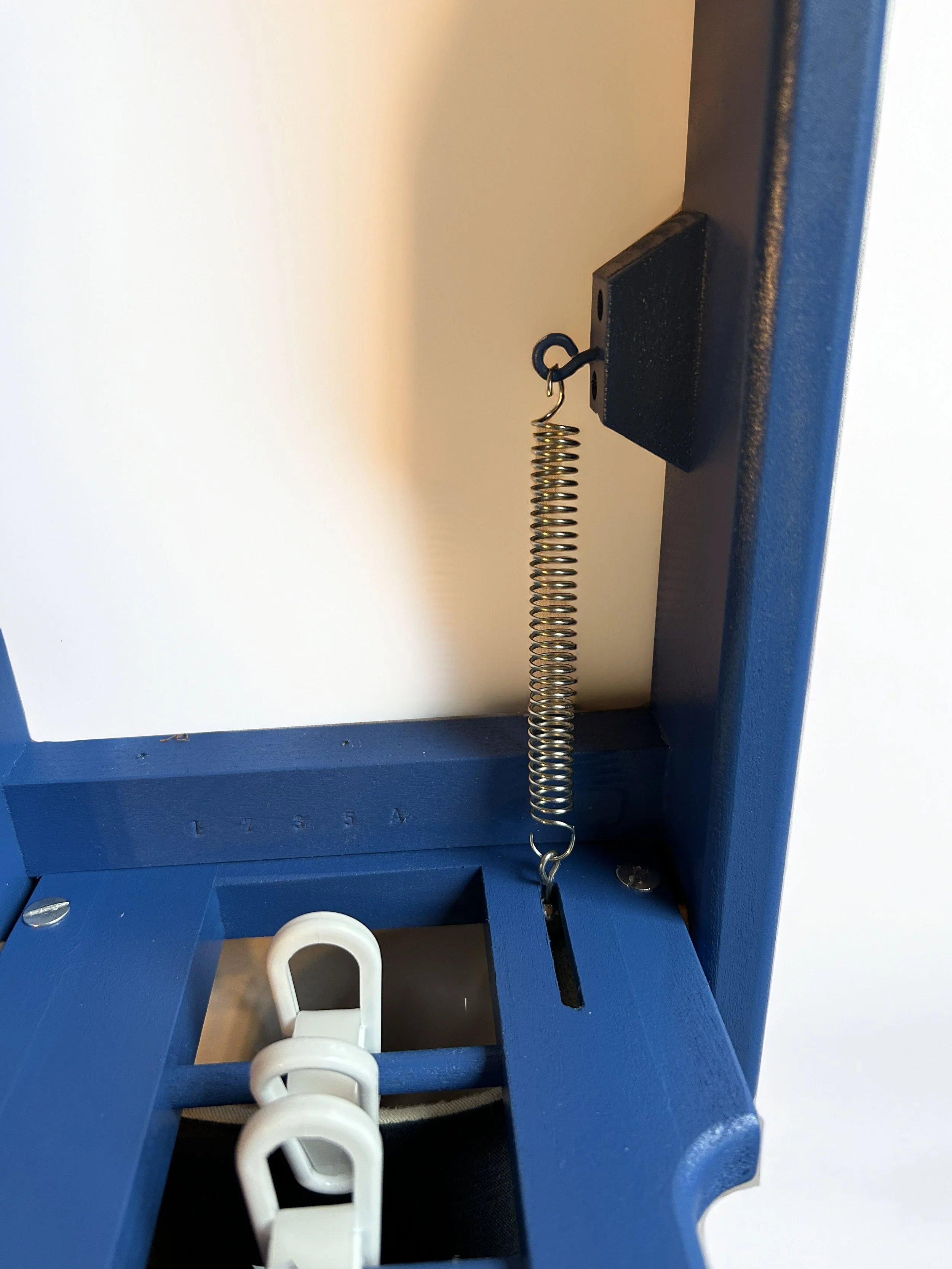 Close-up of a blue framed pinball machine with a metal spring attached to the side and white plastic clips visible.