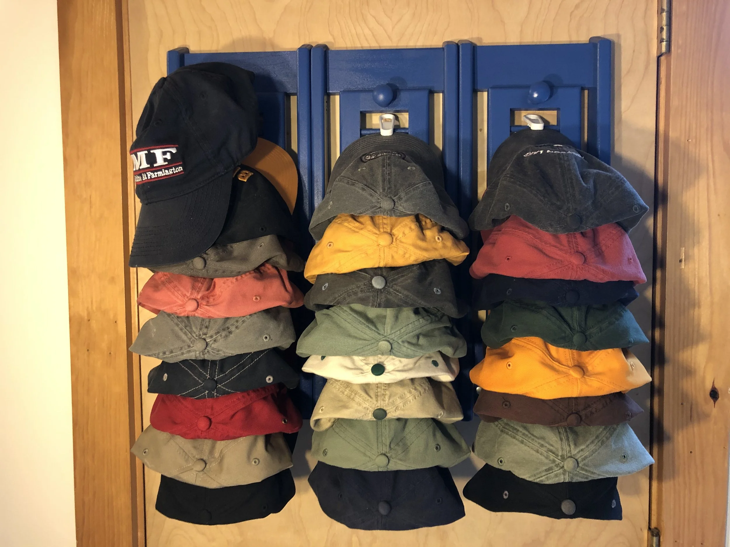 A collection of various colored hats arranged on a blue rack, with a black hat on the left side.