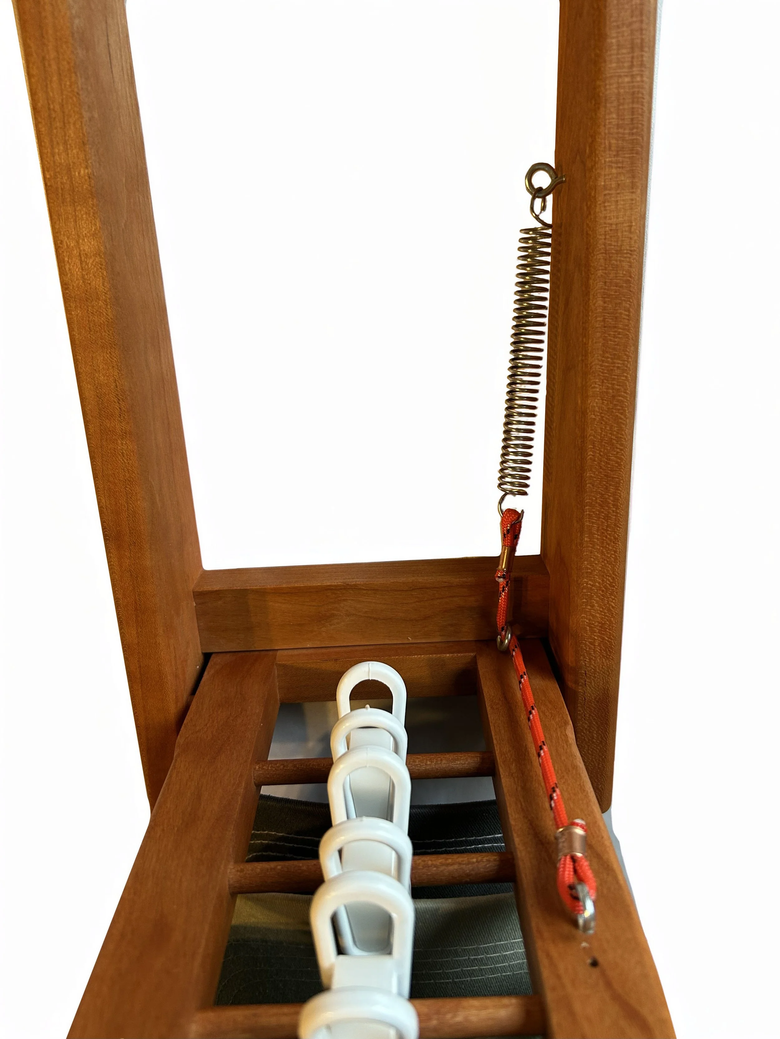 A wooden indoor exercise or stretching apparatus with three white hooks on a black strap and a red and silver resistance band hanging from a metal coil spring.