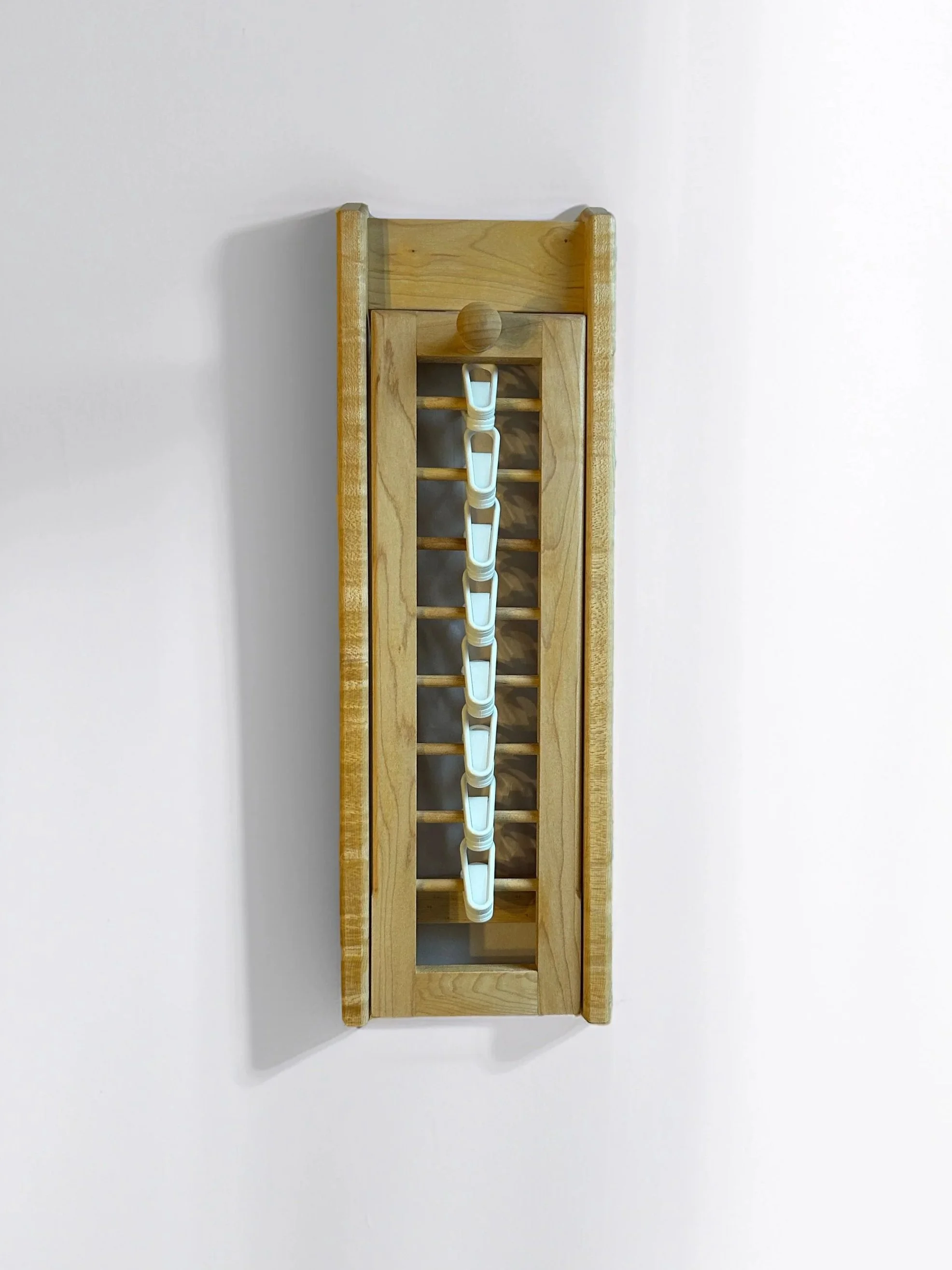 Wooden rack with white plastic clips hanging on it, mounted on a plain white wall.