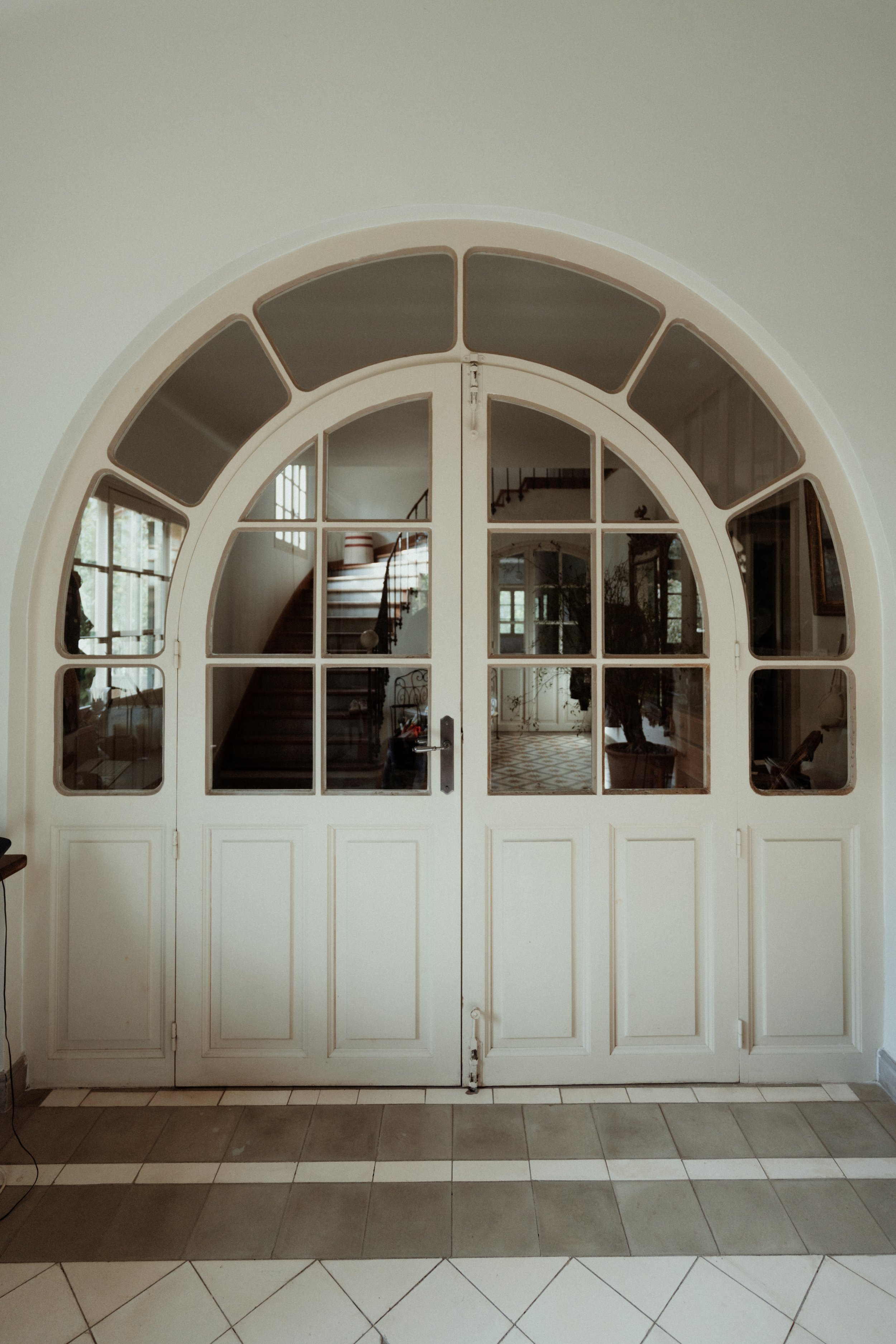Deux portes vitrées avec cadre en bois blanc dans une entrée, avec un escalier en arrière-plan visible à travers les vitres.