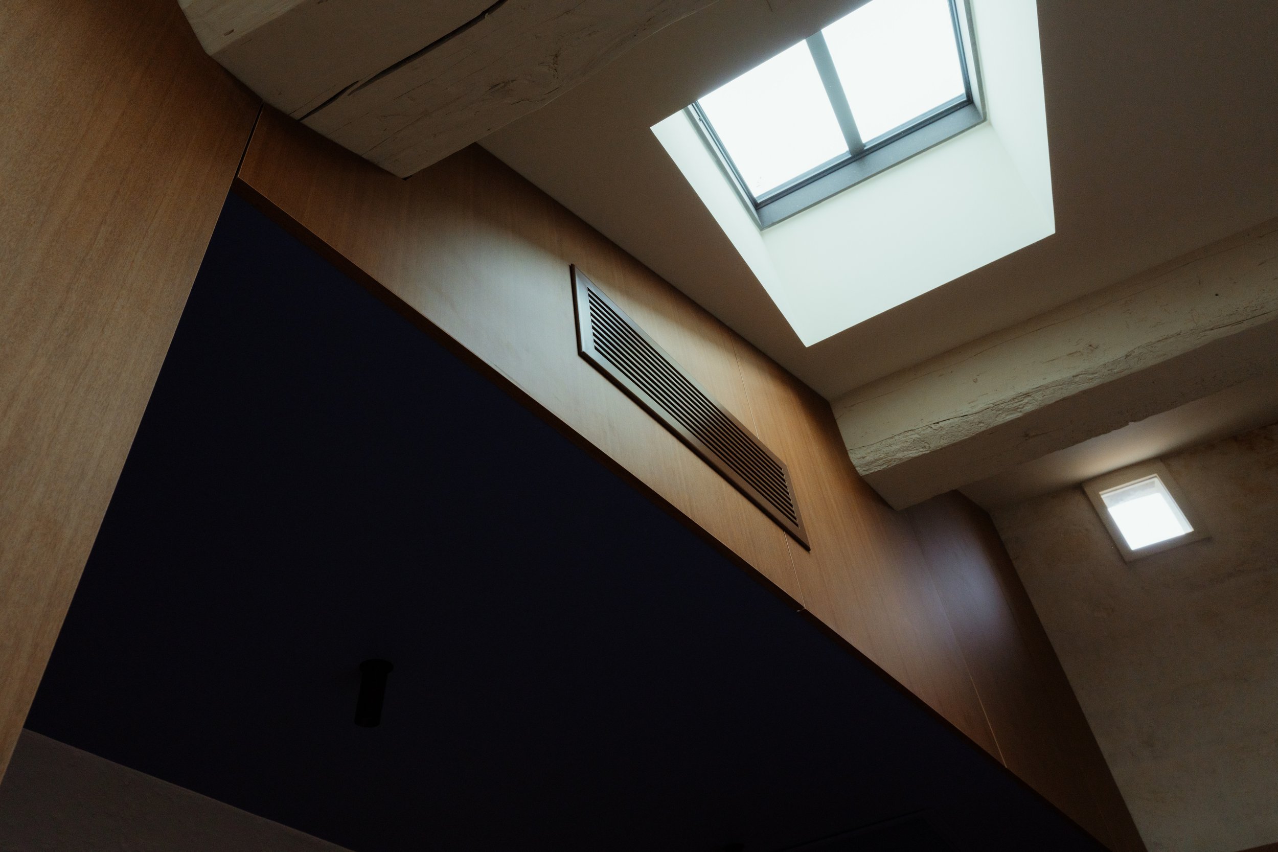 Vue d'un plafond avec une lucarne et une grille de ventilation sur un mur en bois.
