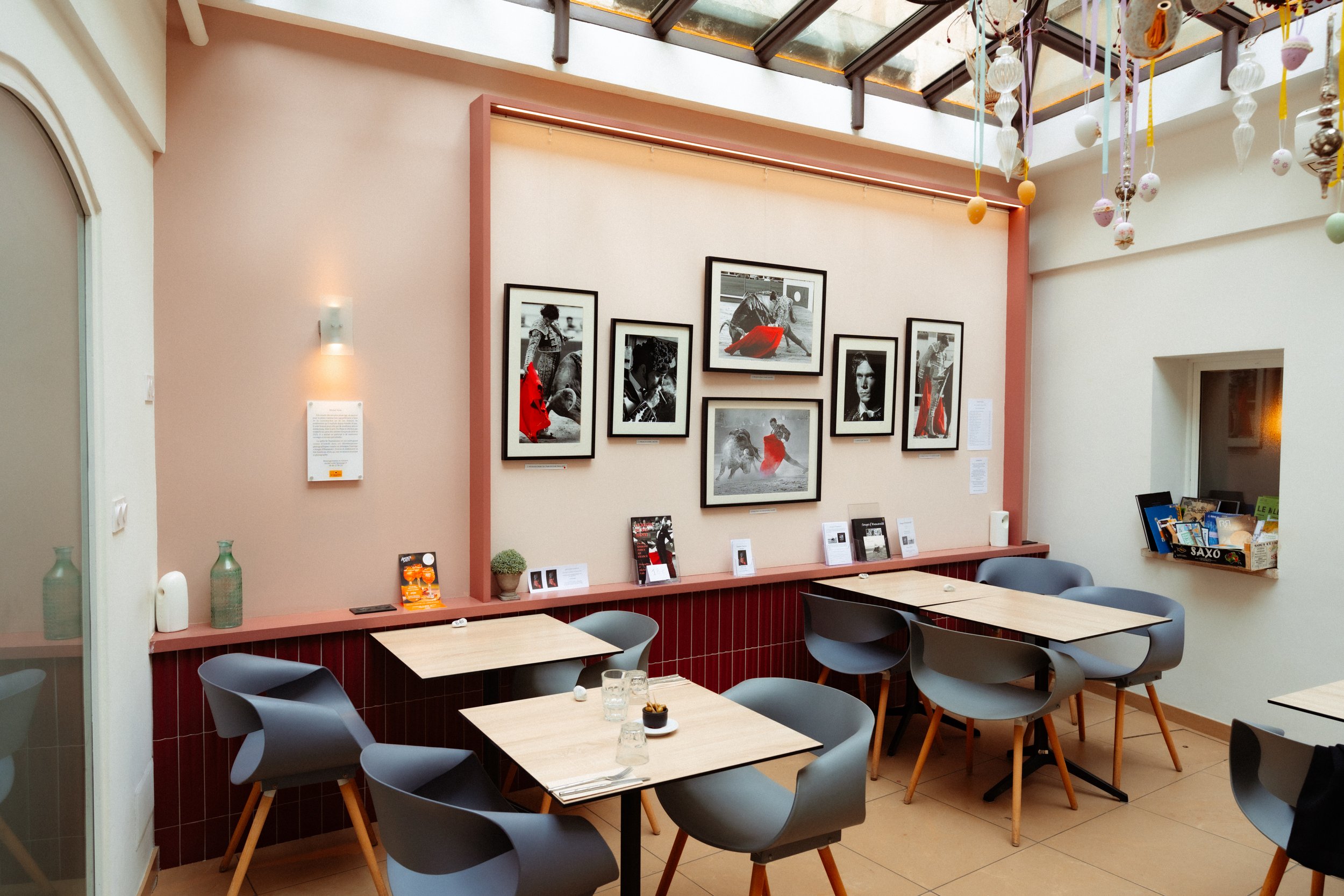 Intérieur d'un café avec tables et chaises modernes, murs décorés de photos en noir et blanc avec accents rouges, et plafond en verre.