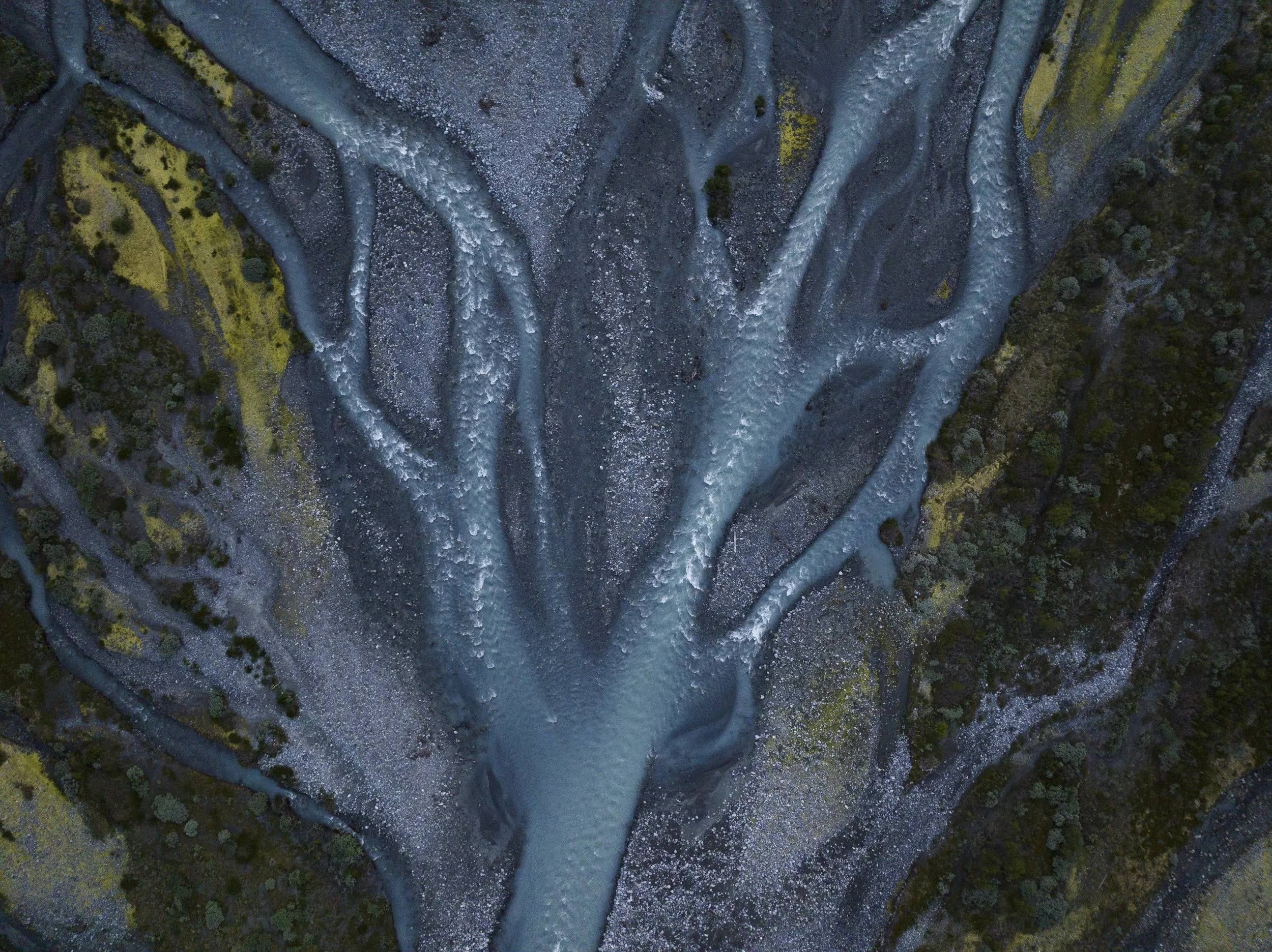 Aerial view of a winding river flowing through a rocky landscape with patches of green trees and shrubs.