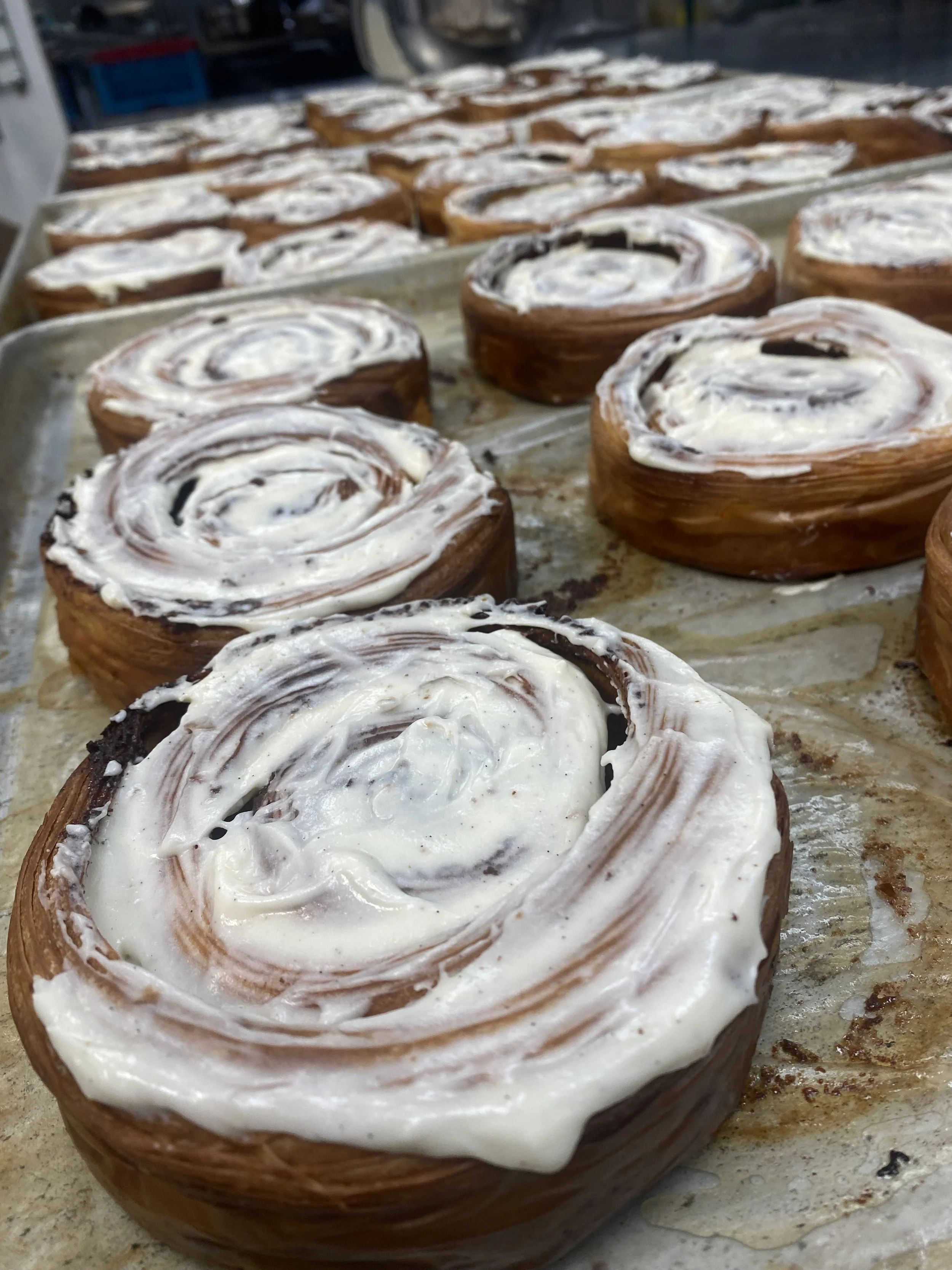 Close-up of baked cinnamon rolls with white icing on a baking sheet.