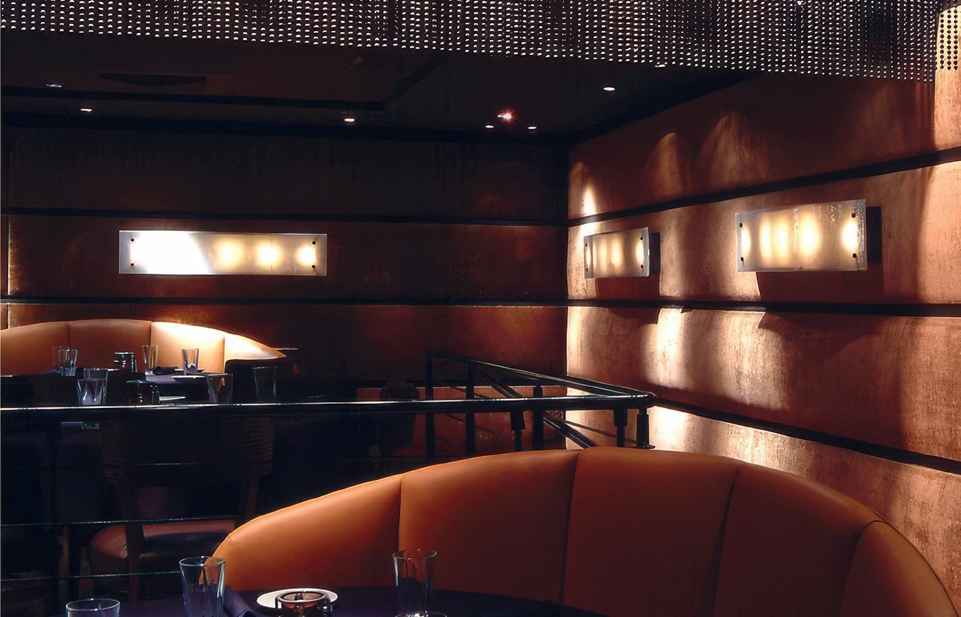 Interior of a dimly lit restaurant with dark walls, illuminated wall sconces, and tables set with glasses and cutlery.