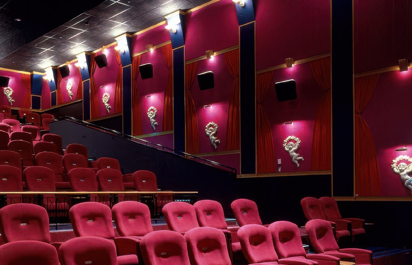 Empty theater with red seats, pink walls, gold accents, and decorative sculptures along the walls.