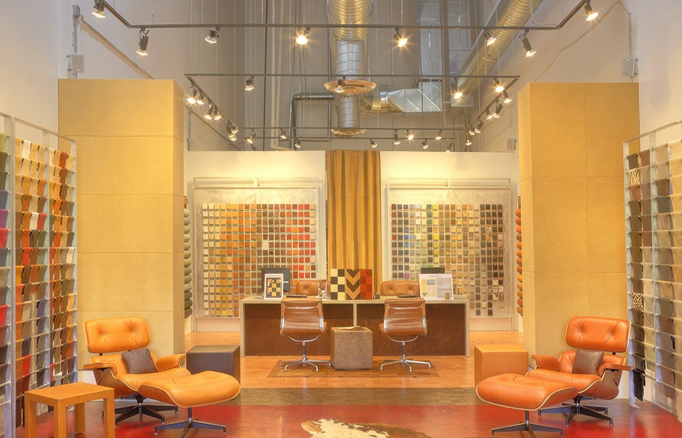 Interior of a fabric and upholstery store with display walls of fabric swatches, orange chairs, and a reception desk.