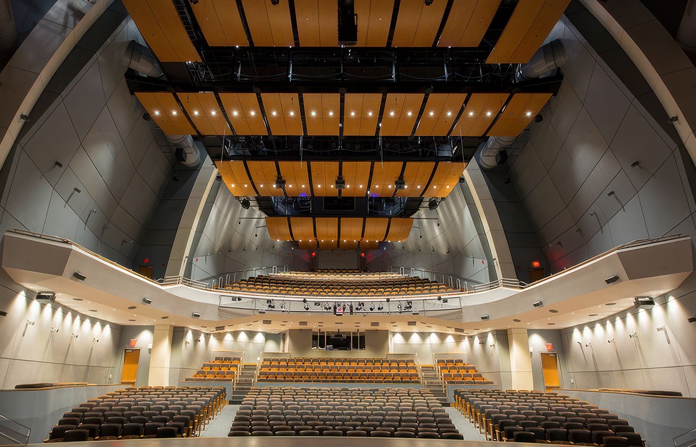 Interior of an empty modern auditorium or concert hall with multiple rows of black and brown seats and wooden ceiling panels.