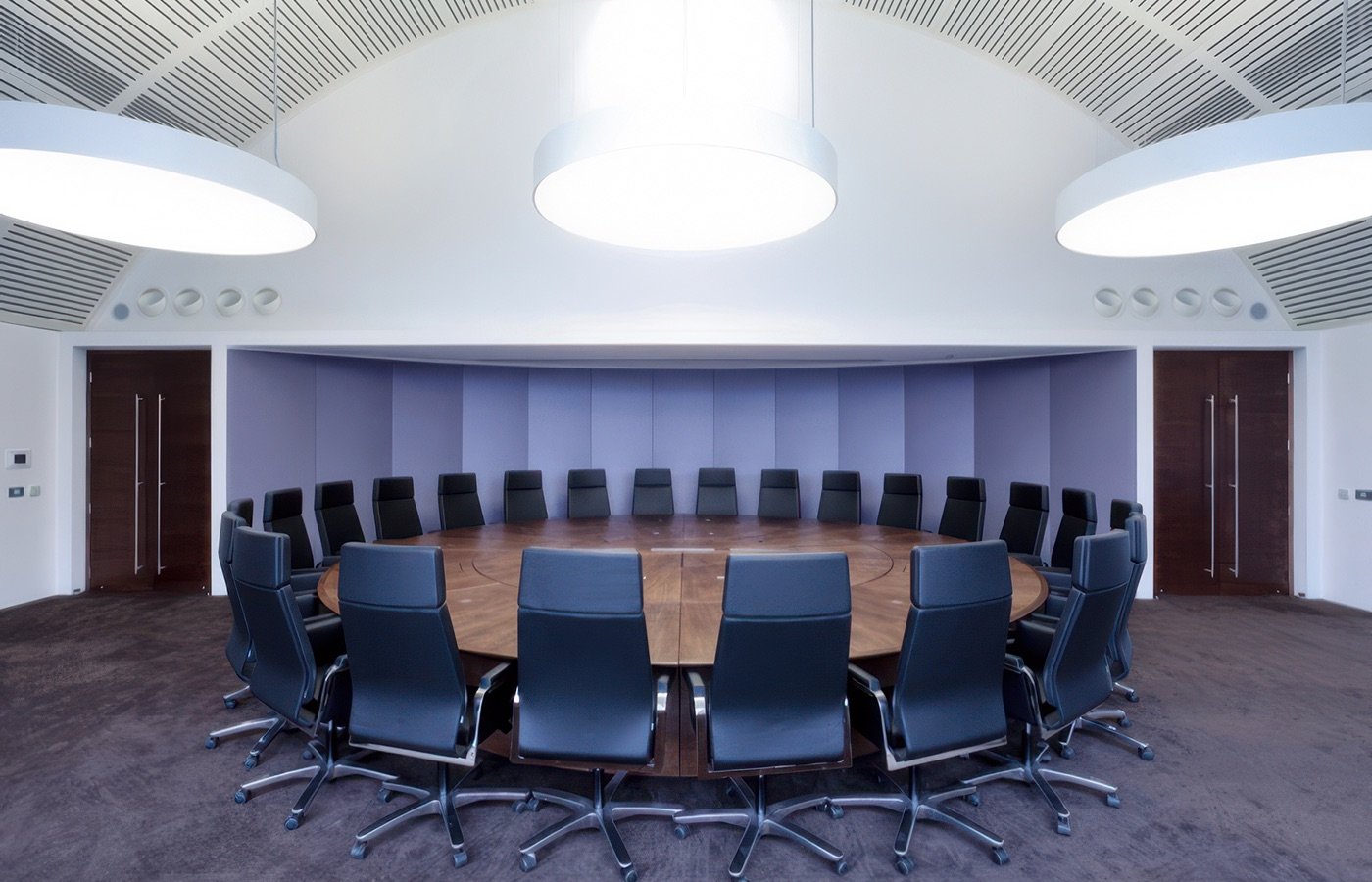 Empty round conference table with 20 black chairs in a modern, bright meeting room.