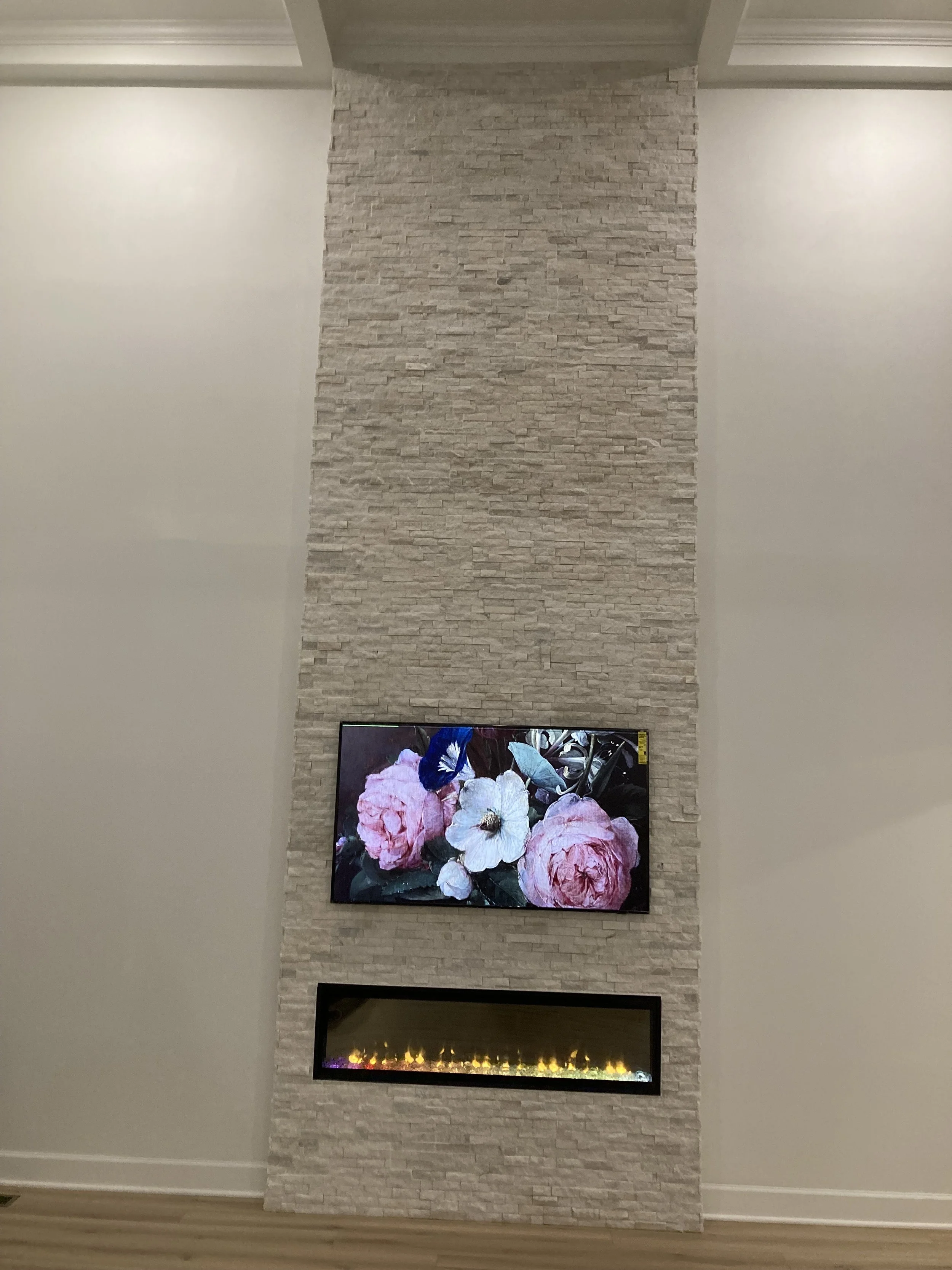 Modern living room interior with a stone-textured wall featuring a mounted TV displaying floral art above a linear electric fireplace.