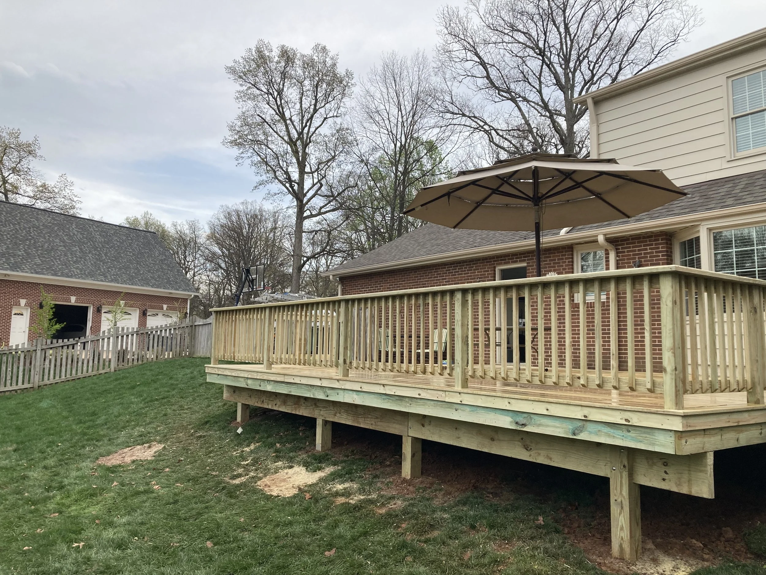 Backyard with wooden deck, patio umbrella, and grass lawn; house and detached garage in background.