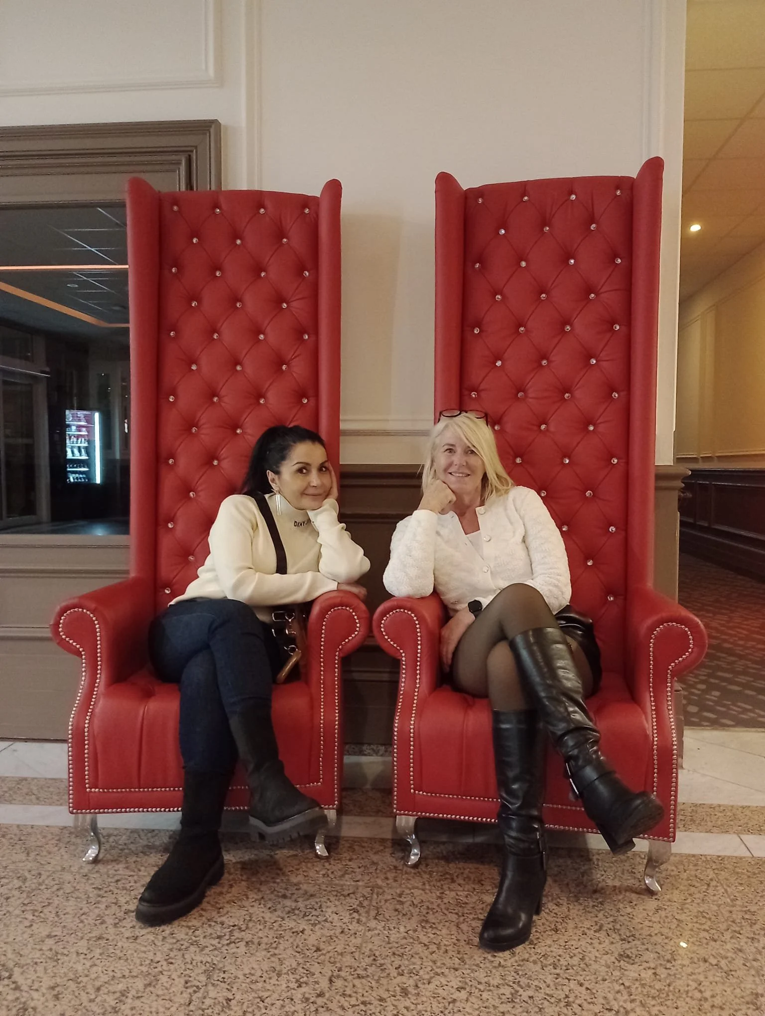 Zwei Frauen sitzen auf großen roten Thronen in einem Hotel Lobbybereich.
