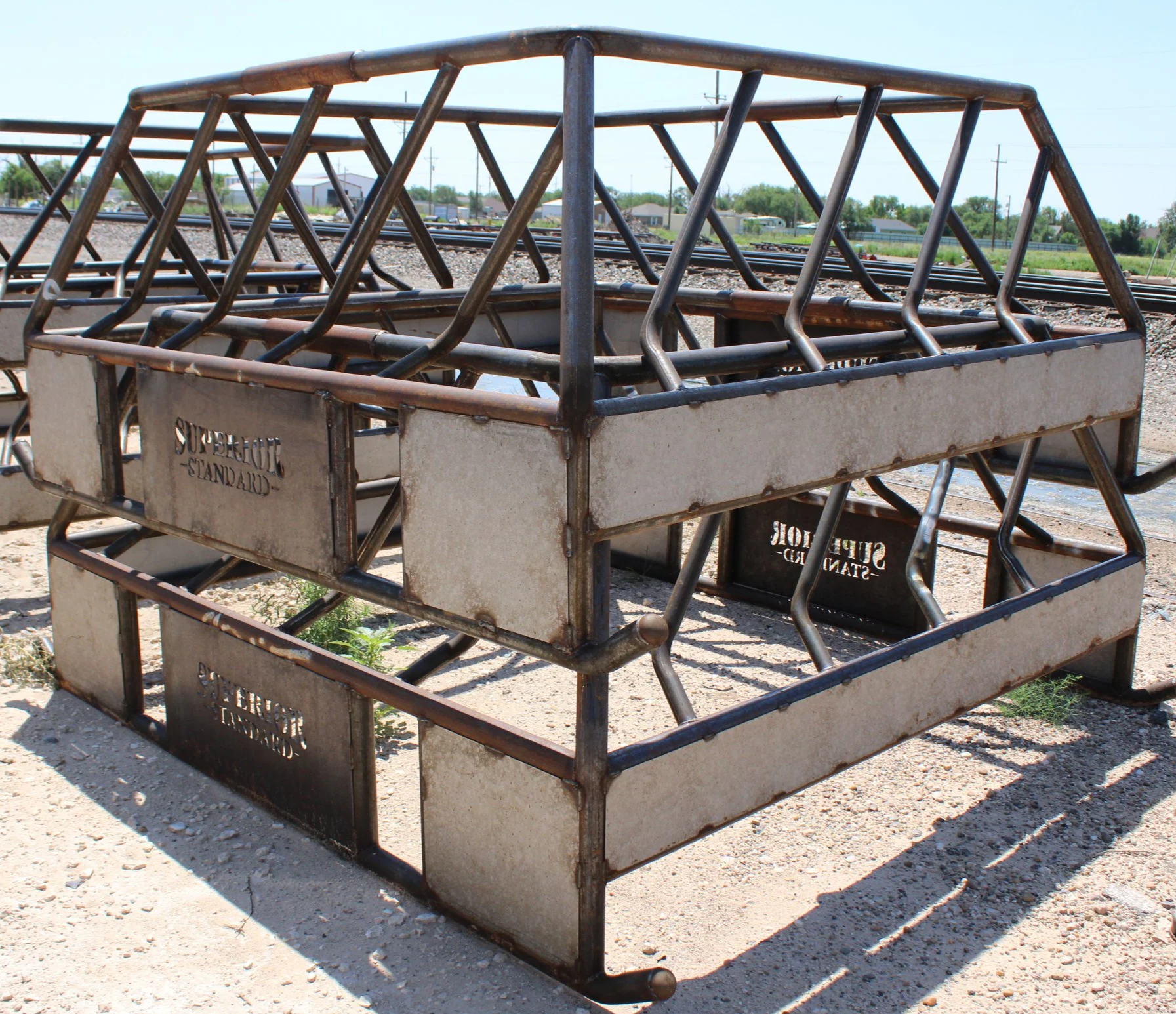 Two metal handcars with the words 'SuperLoc' on the sides, parked on a dirt surface near railway tracks, with a background of trees, buildings, and utility poles under a clear blue sky.