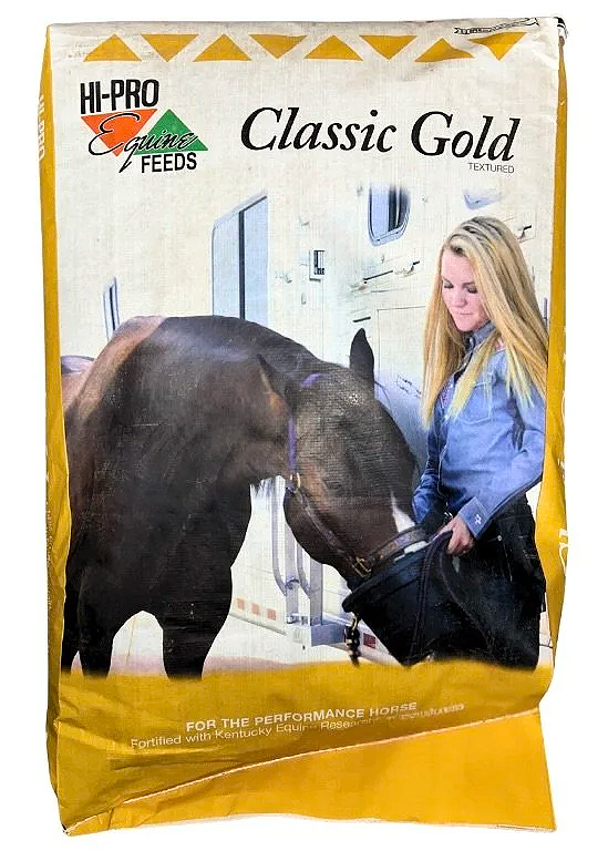 A bag of Hi-Pro Equine Feeds Classic Gold horse feed featuring a woman feeding a brown horse from a black bucket inside a stable.