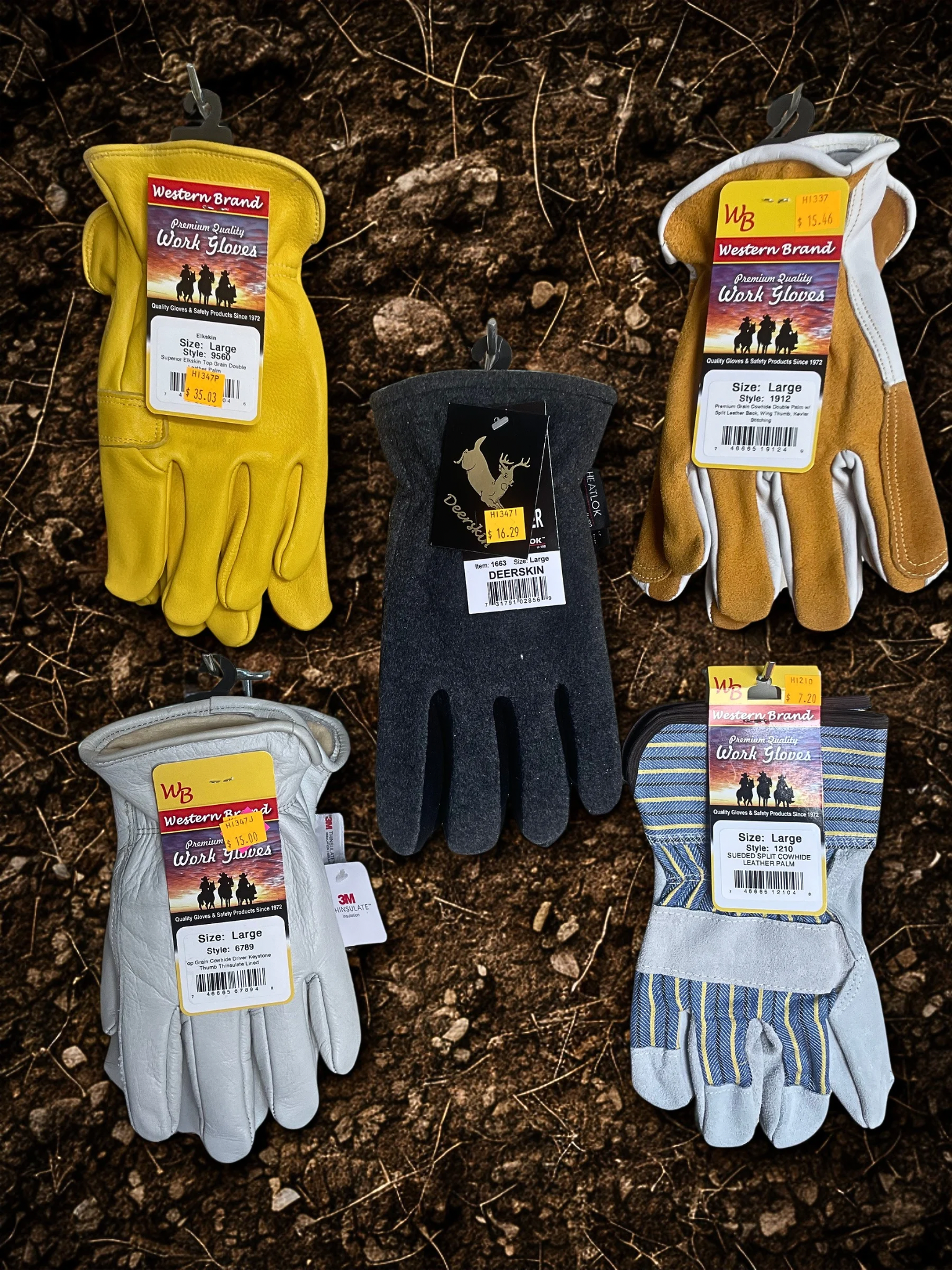 A collection of work gloves displayed on dirt ground. The gloves are different colors and styles, including yellow, black, white, and striped. Each pair is tagged with price labels and branding information.