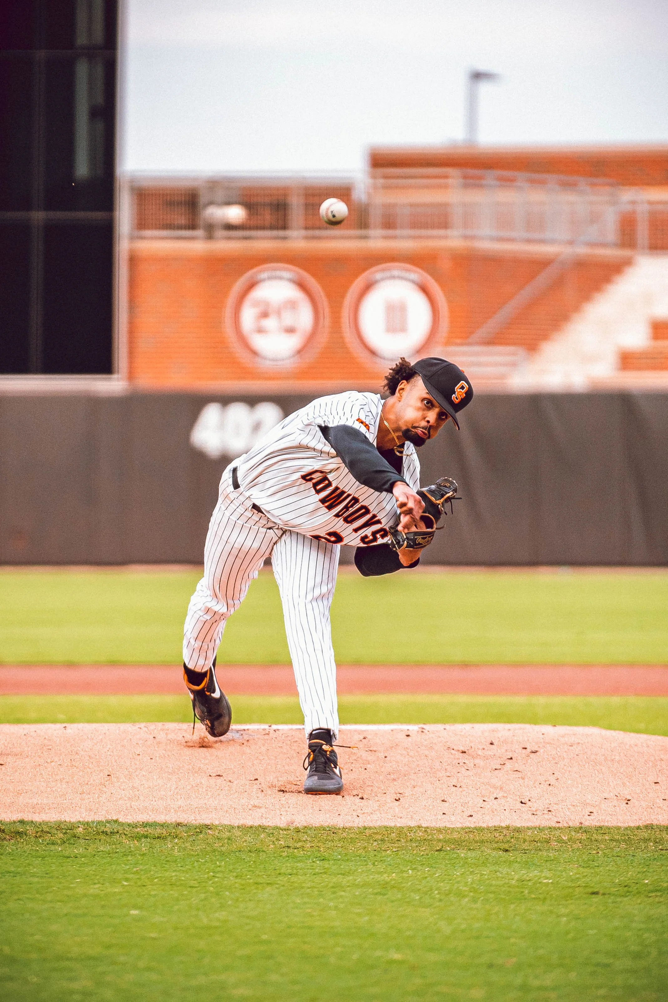 Baseball pitcher in mid-throw on the field wearing a pinstripe uniform with "Cowboys" text and a cap, during a game.