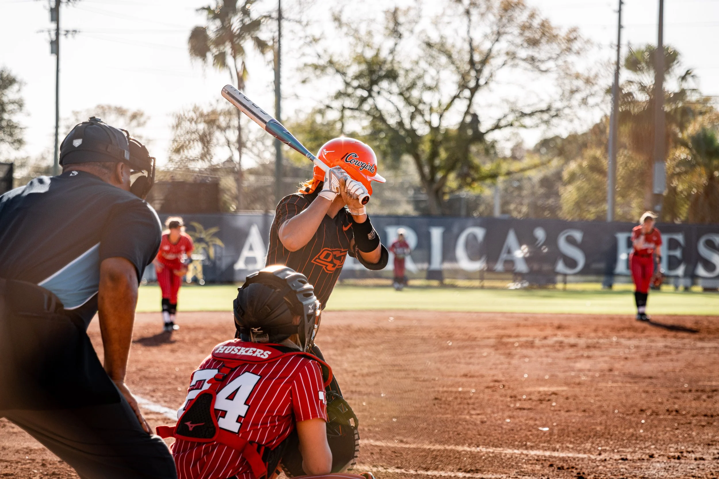 Softball game with batter, catcher, and umpire at home plate.