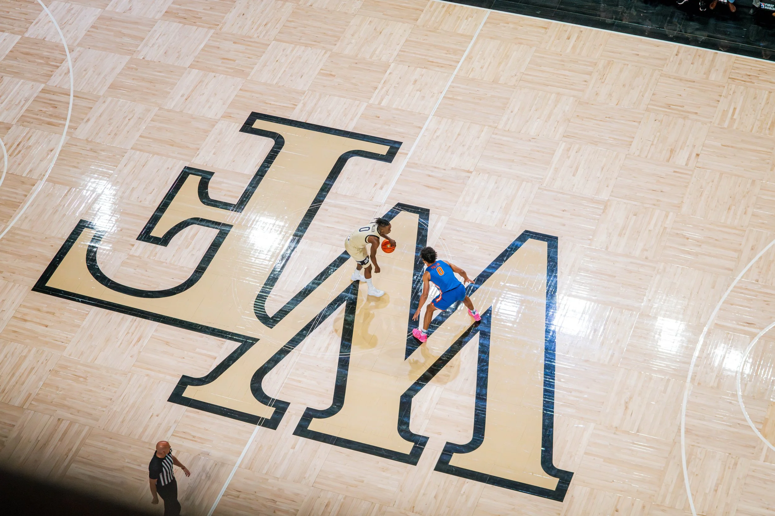 Overhead shot of two basketball players on a court with a large "M" logo in the center.