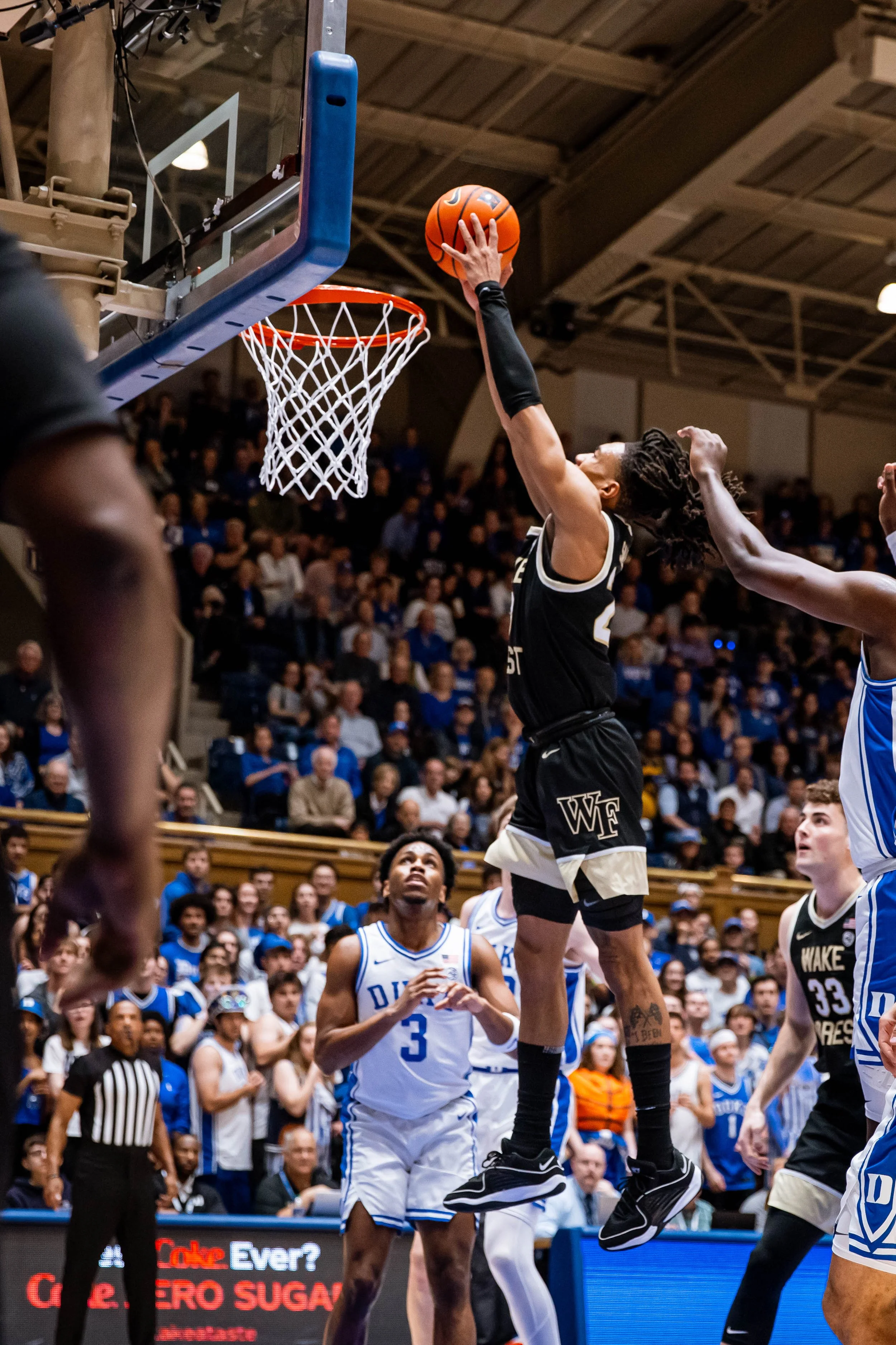 Basketball player from Wake Forest attempting a layup during a game against Duke, with players and spectators in the background.