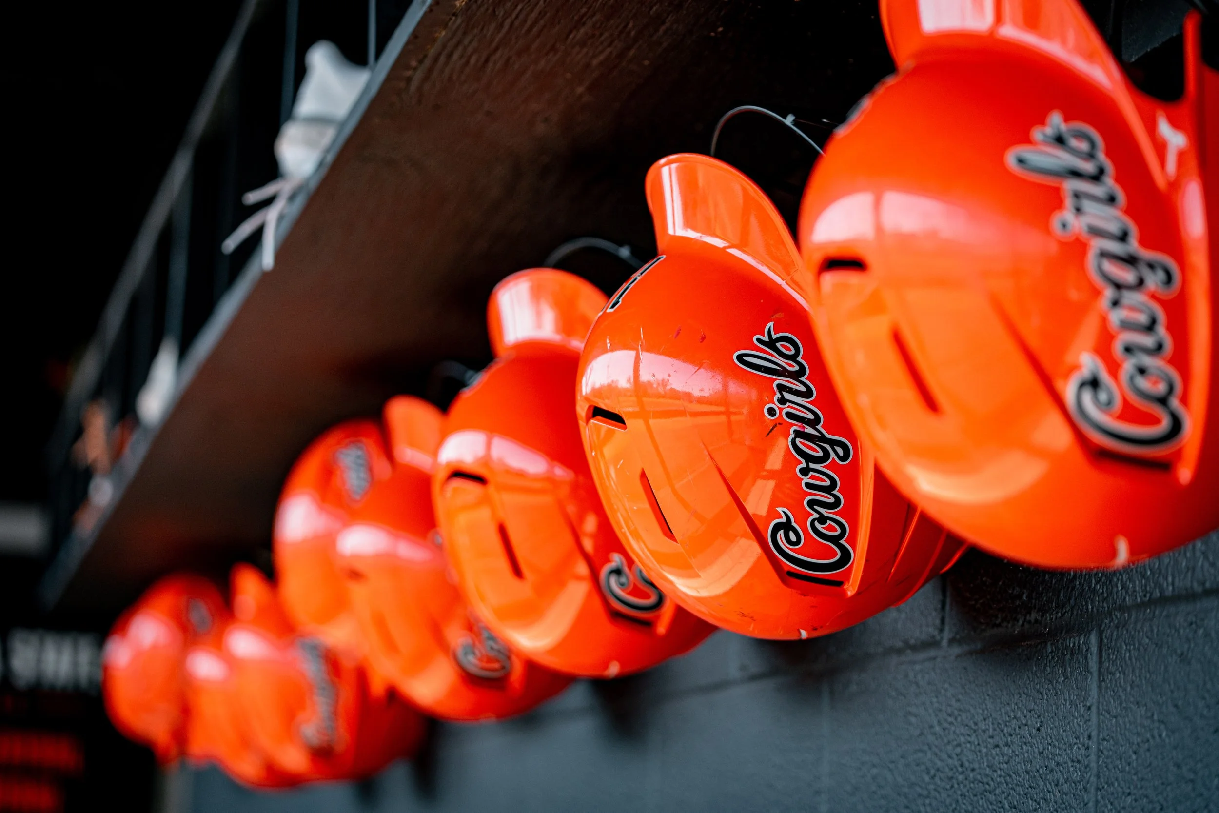 Row of orange baseball helmets with "Cowgirls" text on a wall rack.