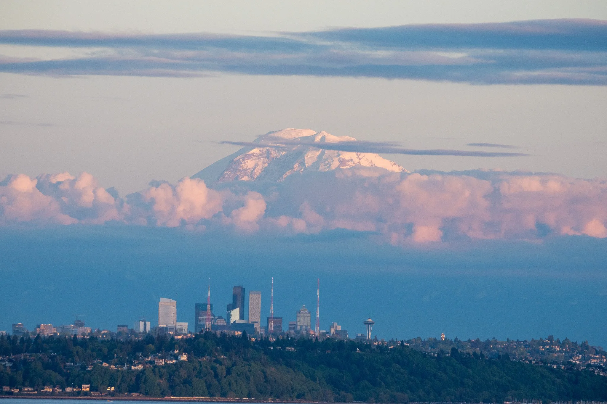 Seattle skyline with Mount Rainier in the background, showing a cityscape with buildings and the Seattle Space Needle beneath snow-capped Mount Rainier with clouds.