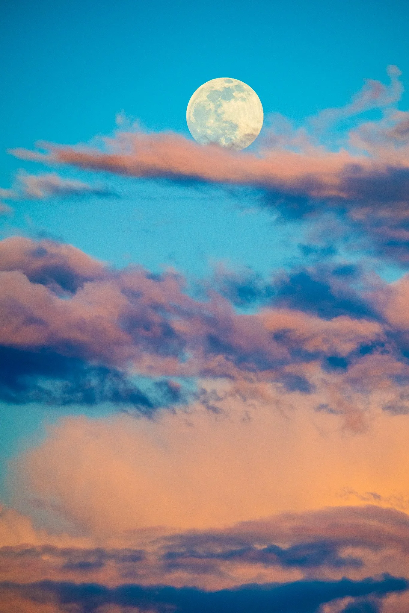 Full moon in a sky with pink and blue clouds.