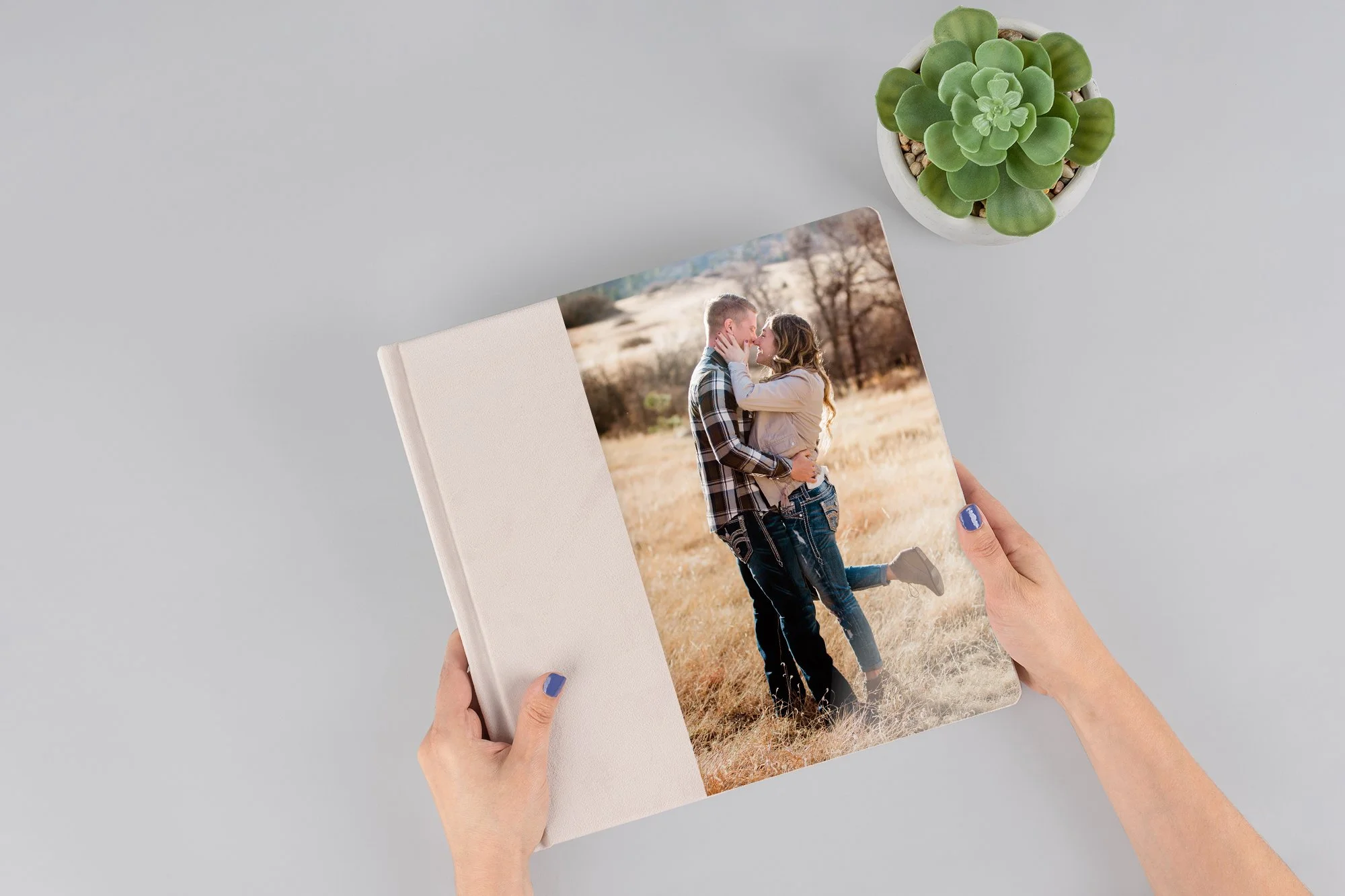 A couple holding hands and walking through a grassy field with mountains in the background, during a cloudy day.