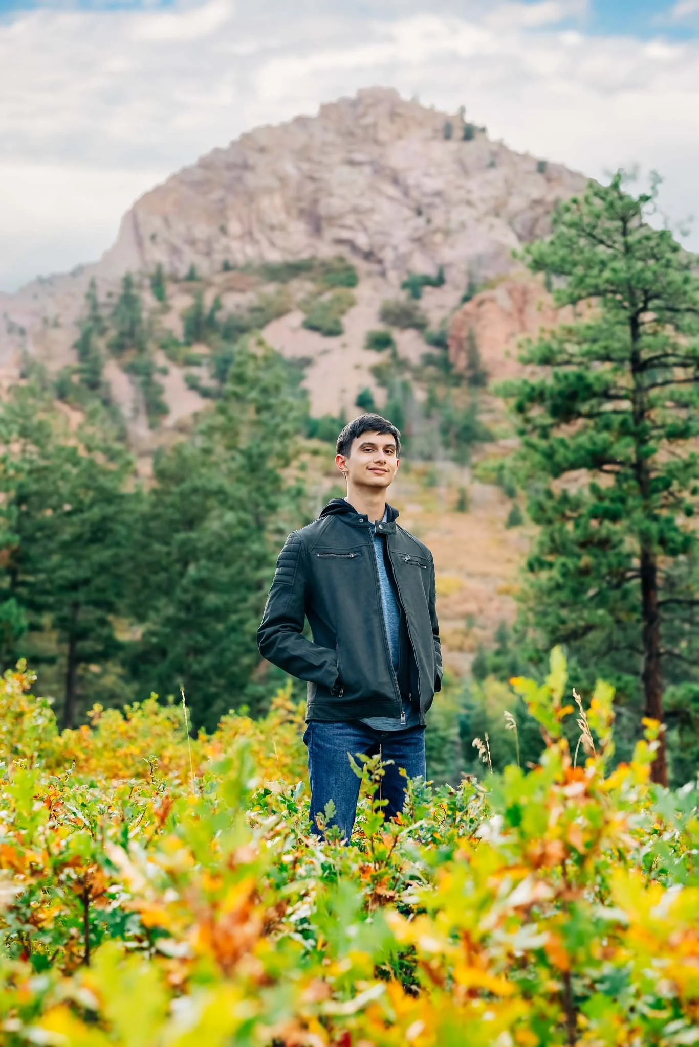 Young man standing in a lush garden with mountains and trees in the background
